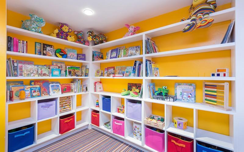 Children’s playroom with white shelves filled with books, toys, and colorful storage bins.