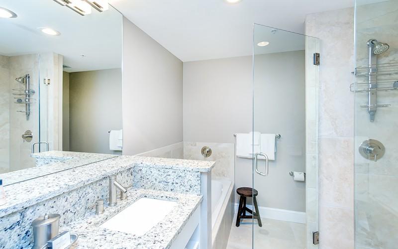 Bathroom with a speckled stone double vanity and glass-enclosed shower.