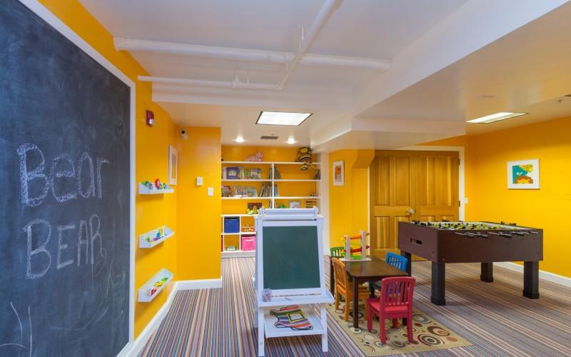 Playroom with a foosball table, child-sized furniture, toy shelves, and a large chalkboard.