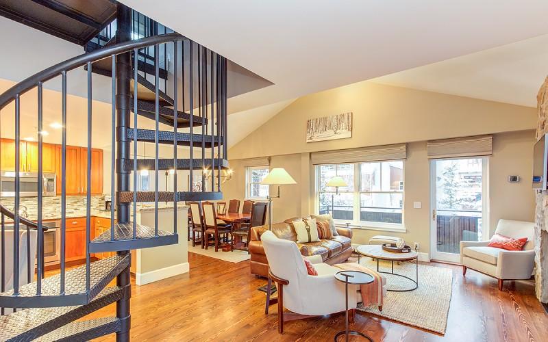 Open-plan living and dining room with a black spiral staircase and bright orange kitchen.