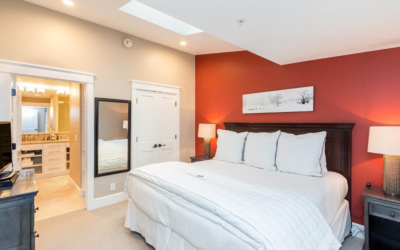 Bedroom with white bedding, a red accent wall, and an open doorway to a bathroom.