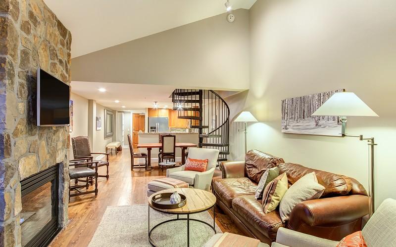 Living room with a stone fireplace, leather sofa, and spiral staircase.