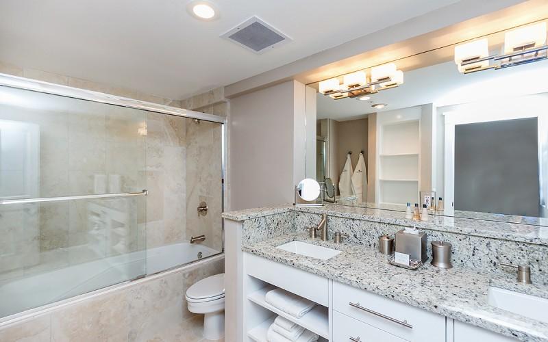 Bathroom with a glass-enclosed tub and shower and a granite double vanity.
