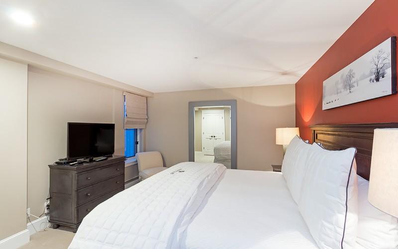 Furnished bedroom with a white bed, dark wood headboard, and rust-red accent wall.