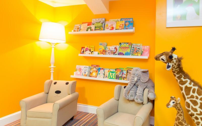 Children’s reading nook with book shelves, cream armchairs, a plush elephant, and giraffe decorations.
