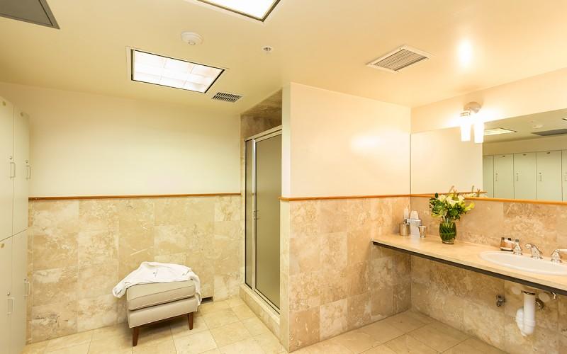 Bathroom with a glass shower, stone-tiled walls, long vanity, and towel-covered cushioned bench.