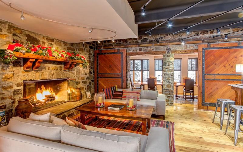 Living room with a stone fireplace, exposed beams, and large sliding wood doors.