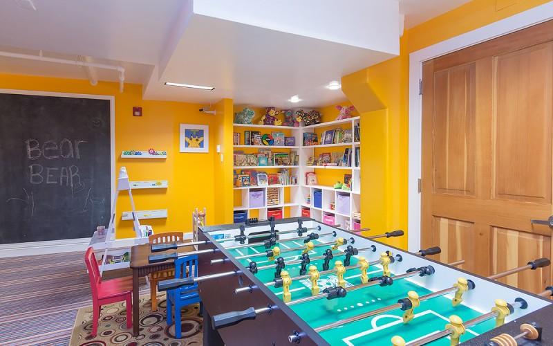 Game room with two foosball tables, bright yellow walls, and shelves of books and toys.