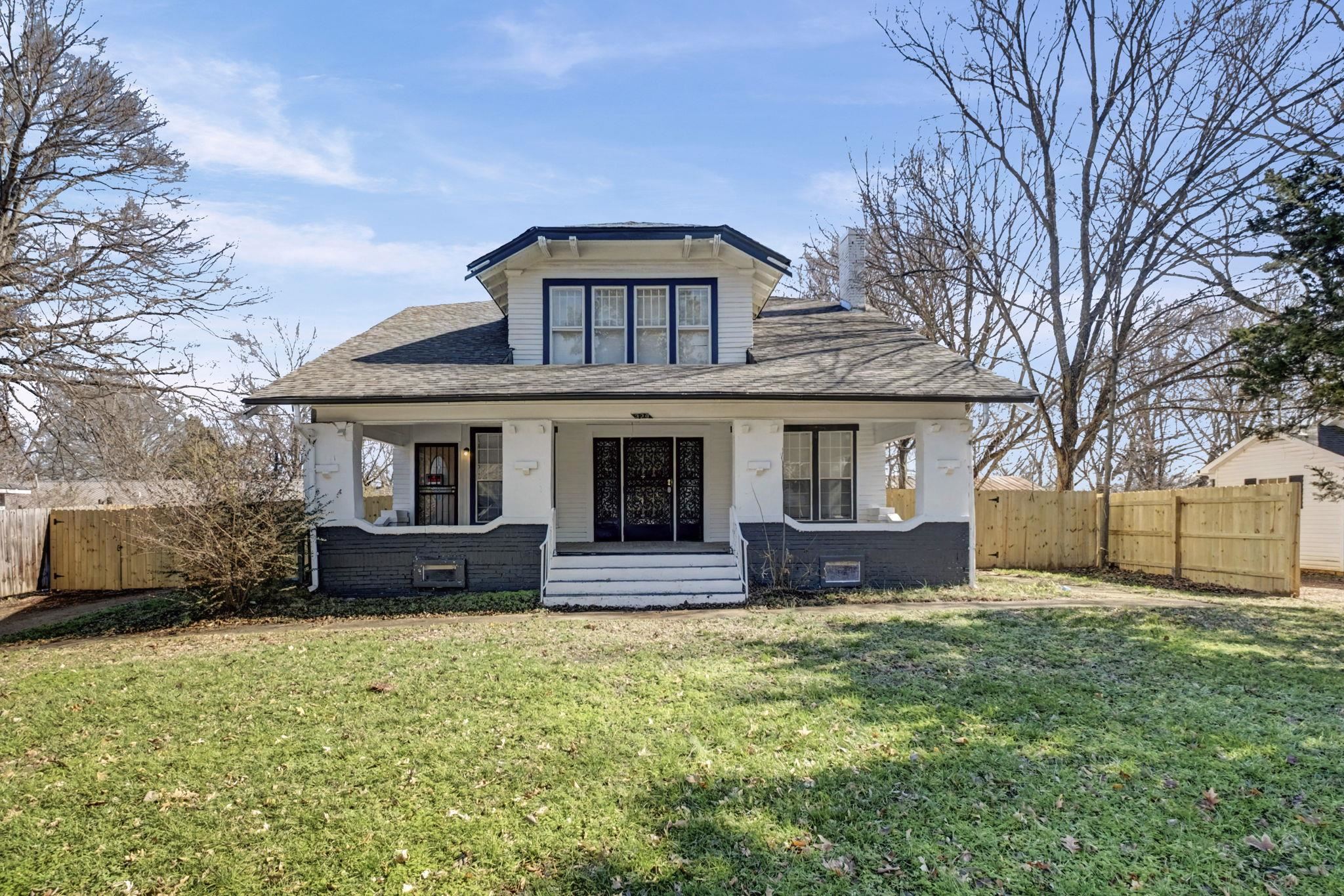 White two-story house with a covered porch, decorative black entry doors, and a fenced yard.
