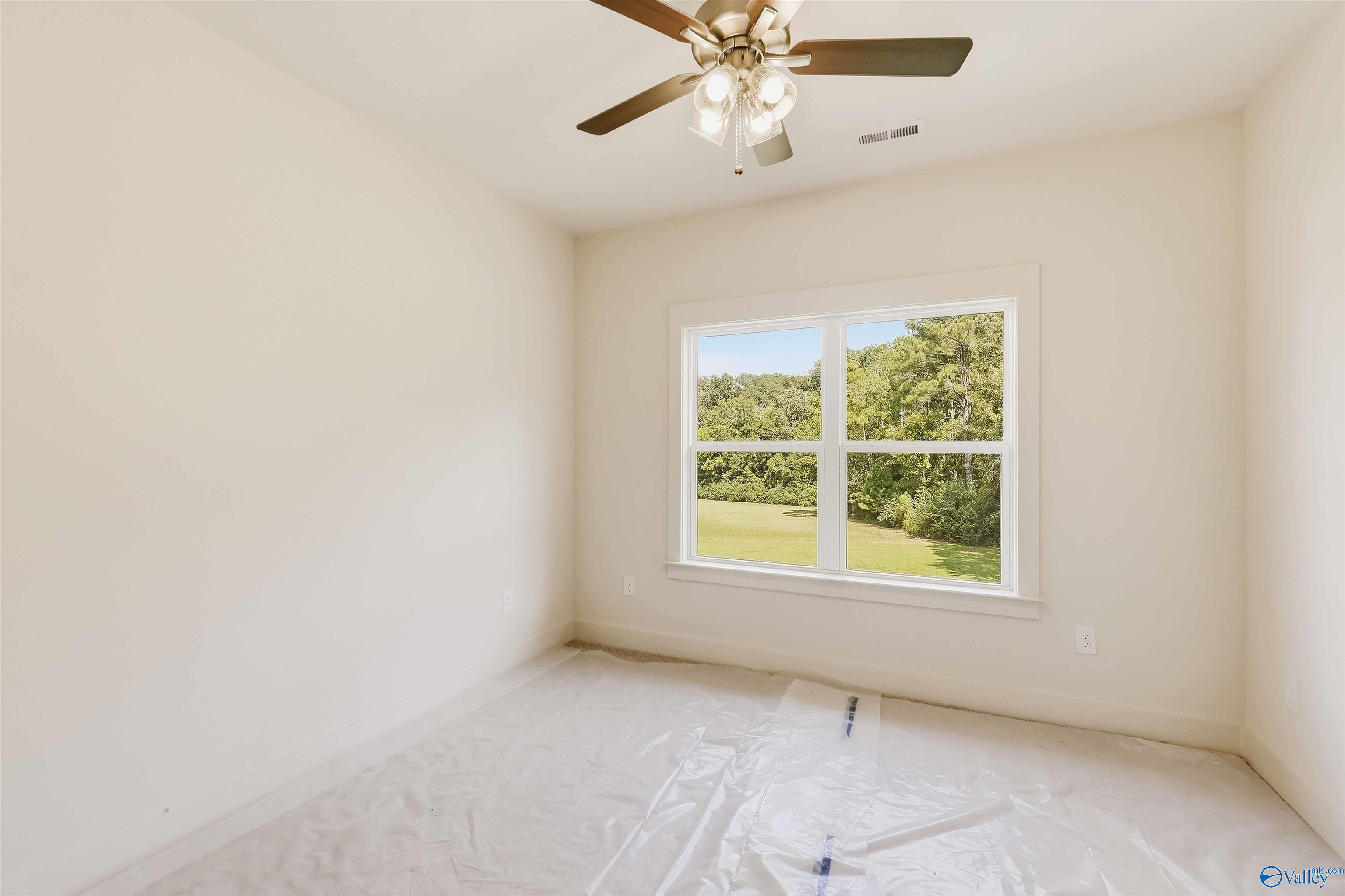 Vacant room with a ceiling fan and large window overlooking a green lawn and trees.