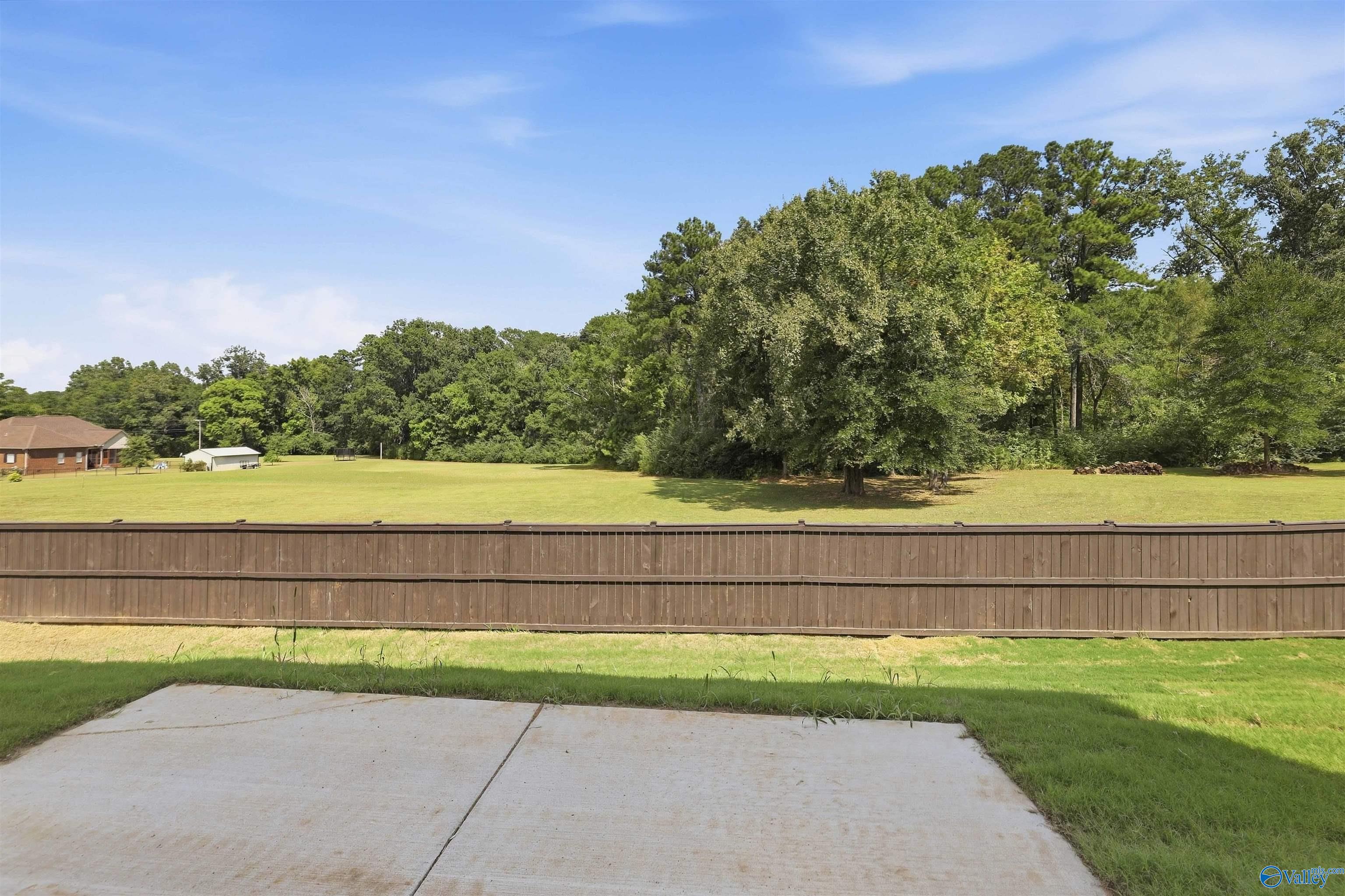 Backyard with a concrete patio, long wooden fence, open lawn, and mature trees.