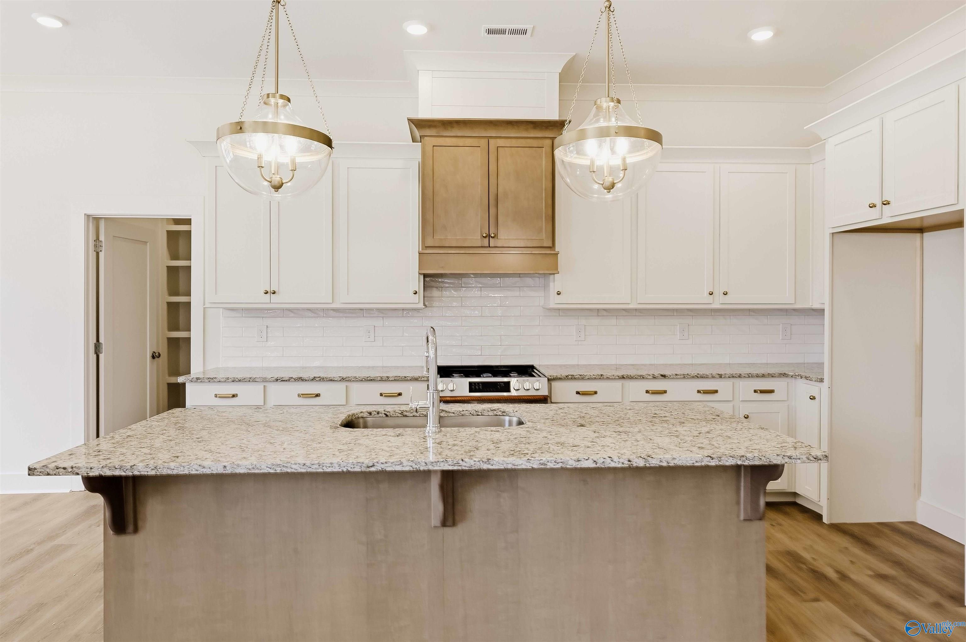Kitchen with a large granite island, white cabinetry, tile backsplash, and glass pendant lights.