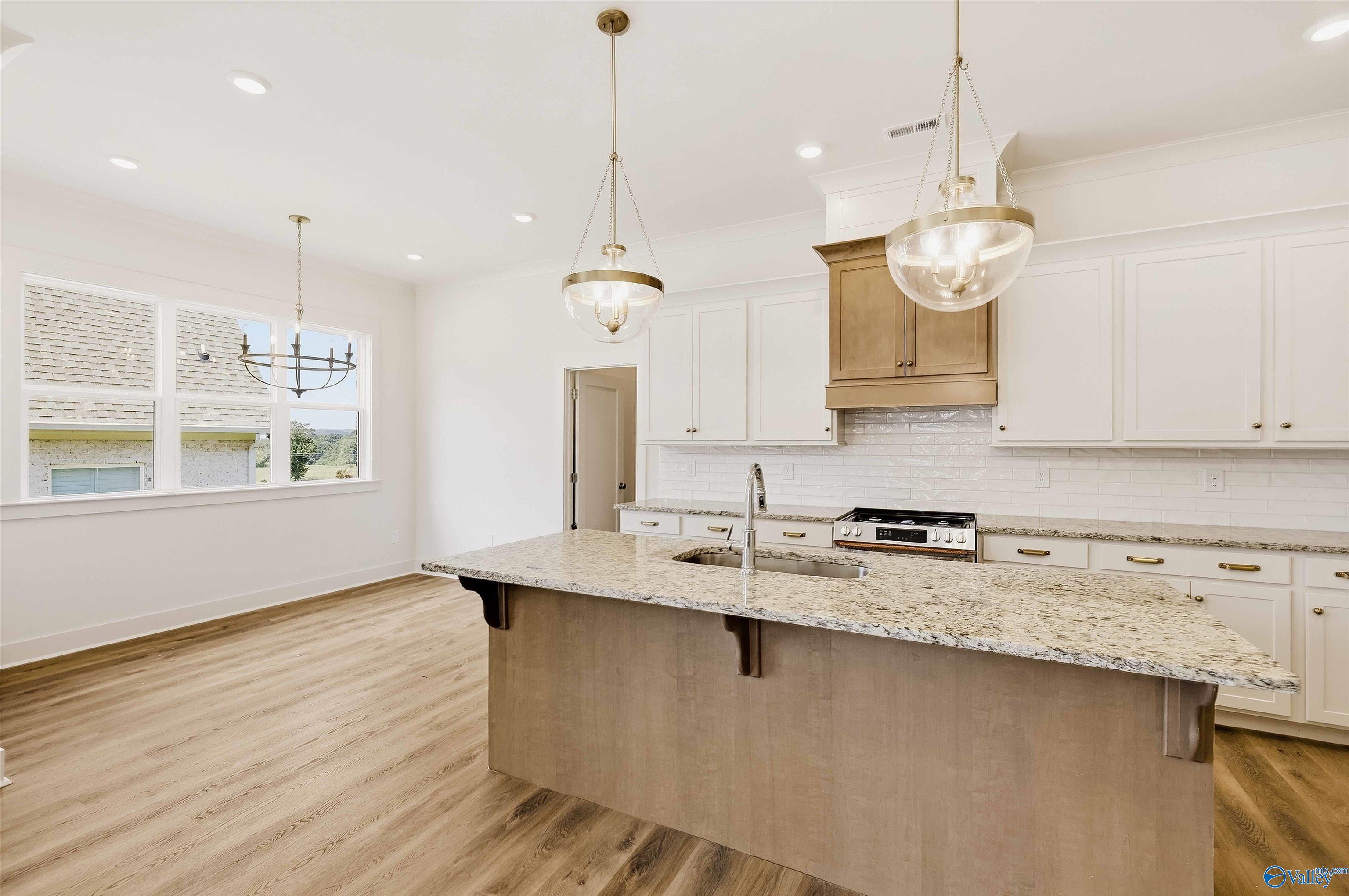 Bright kitchen with a large granite island, white cabinets, and pendant lights.