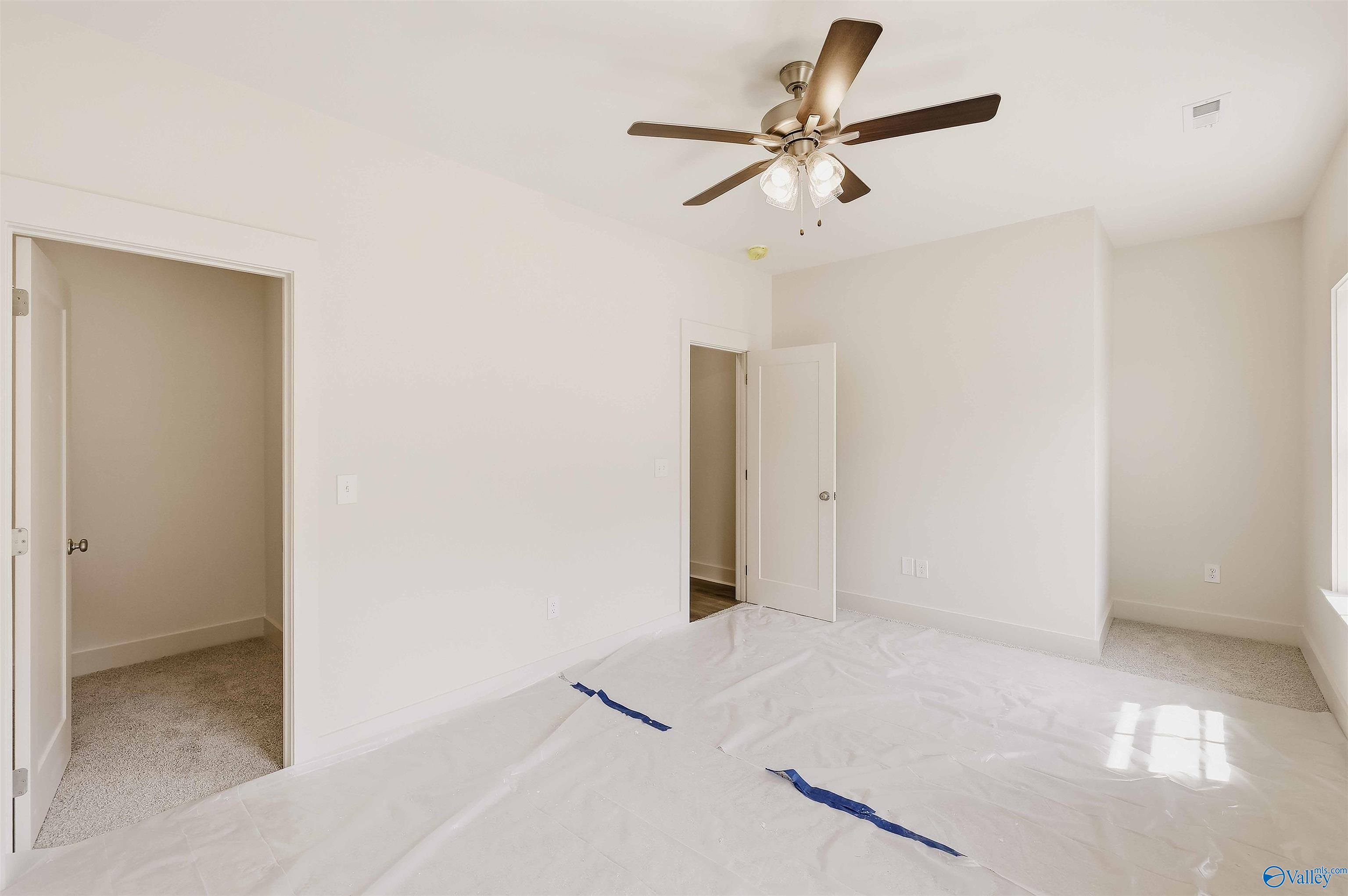 Empty bedroom with a ceiling fan, carpeted closet, and protective floor covering.