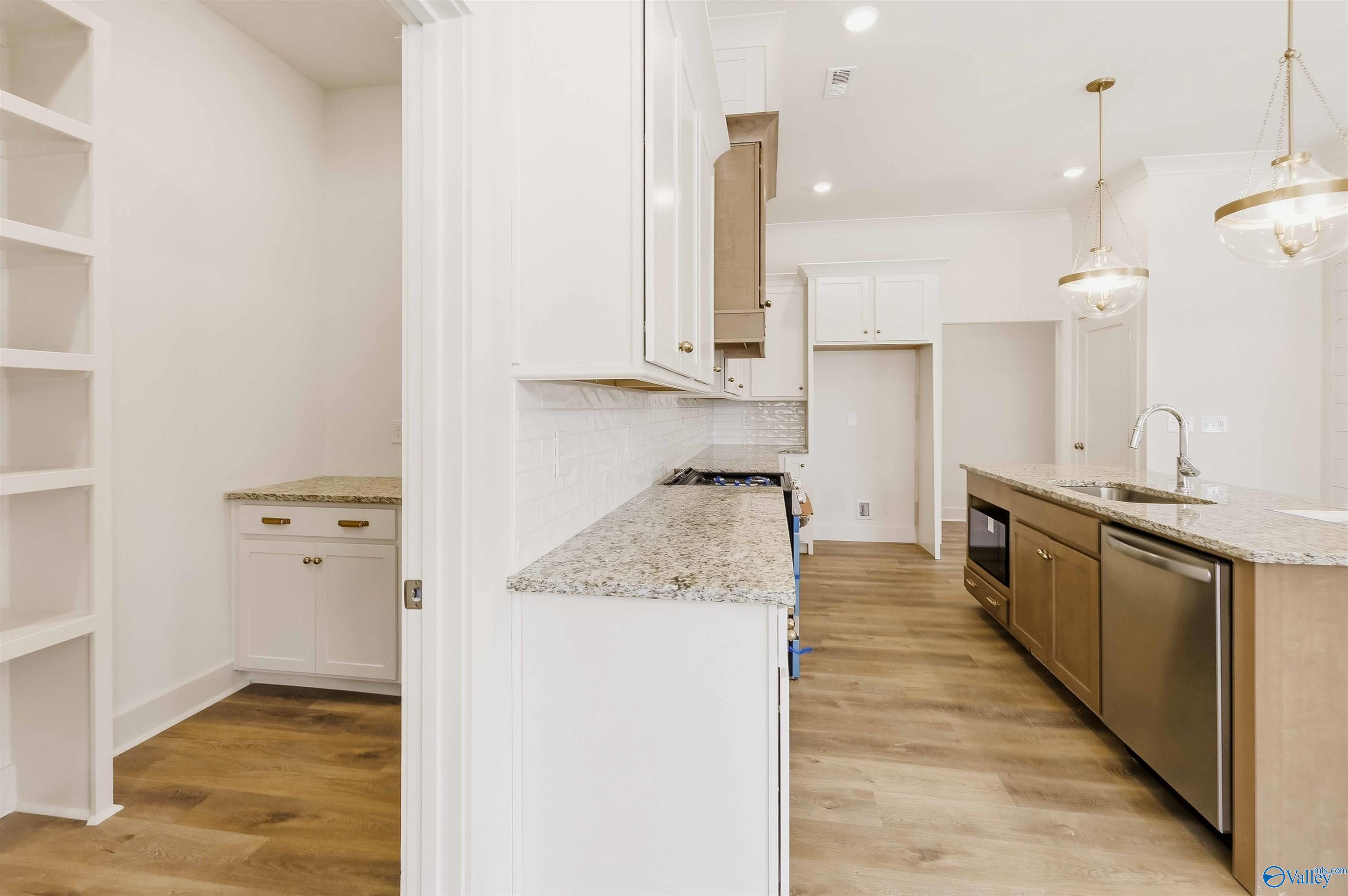 Kitchen with a granite island, sink, dishwasher, white cabinetry, and open shelving.