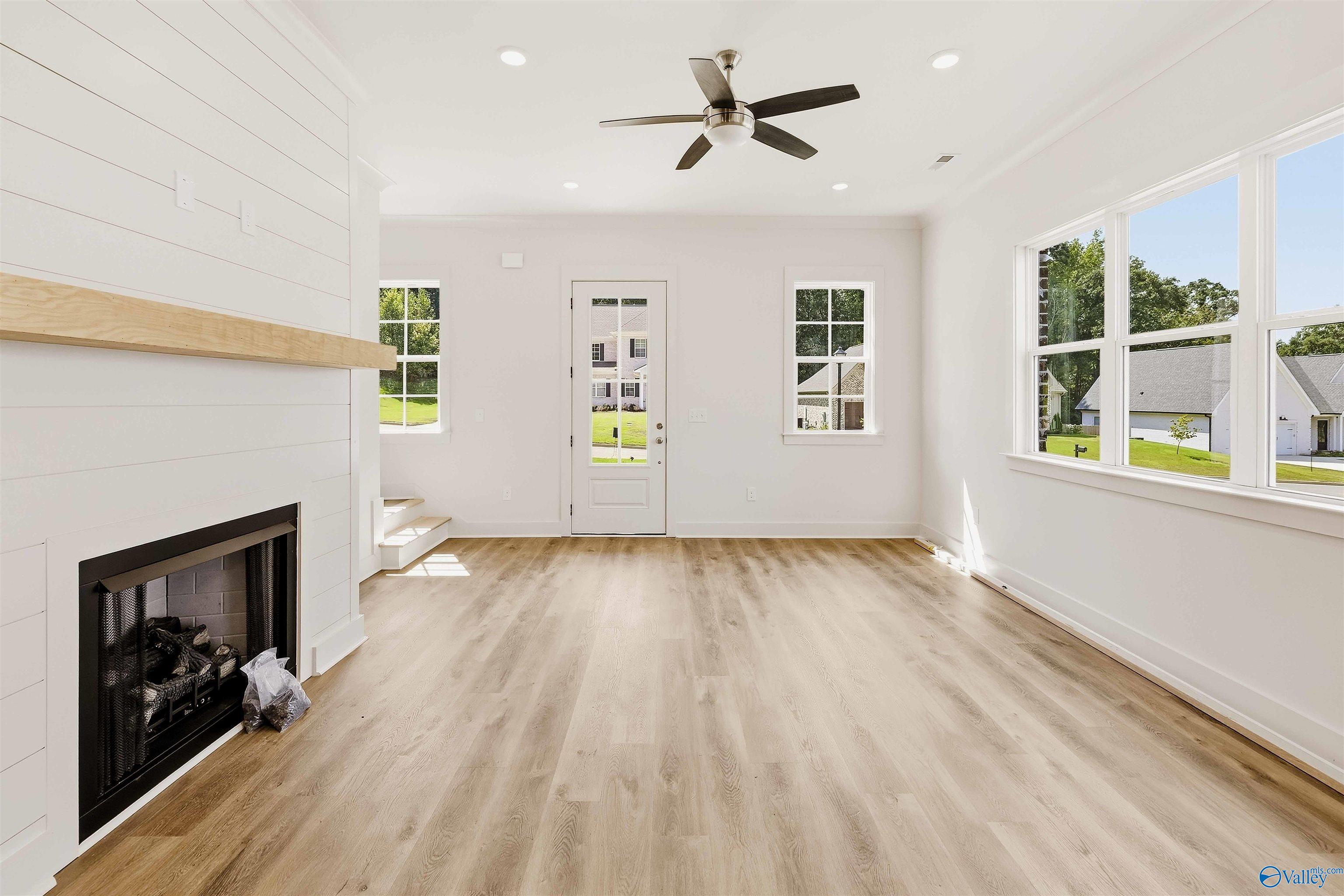 Vacant living room with a white fireplace, light wood floors, and large windows.