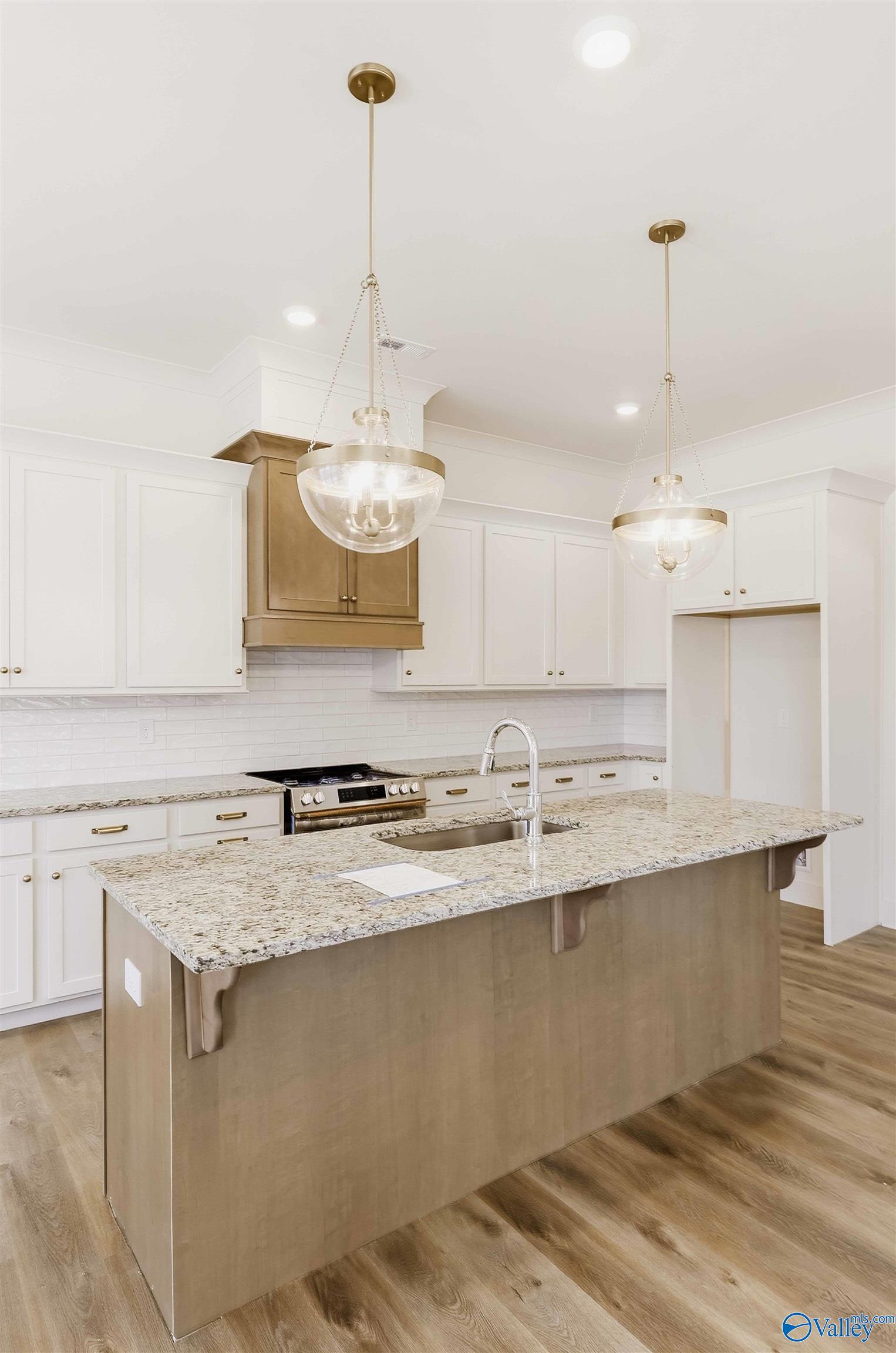 Kitchen with a granite-topped taupe island, white cabinets, and glass pendant lights.