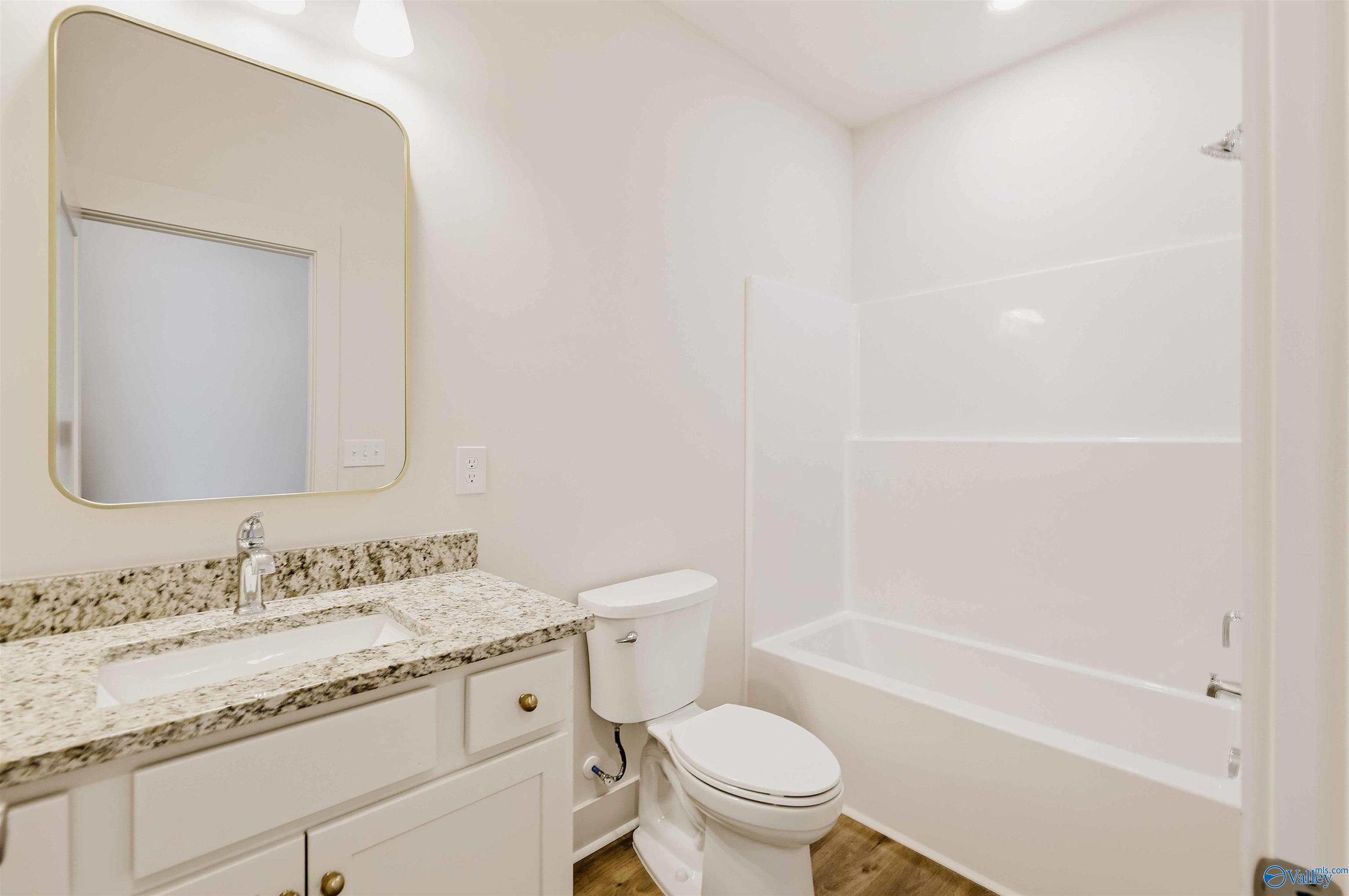 Bathroom with granite vanity, rounded mirror, toilet, and white tub-shower.