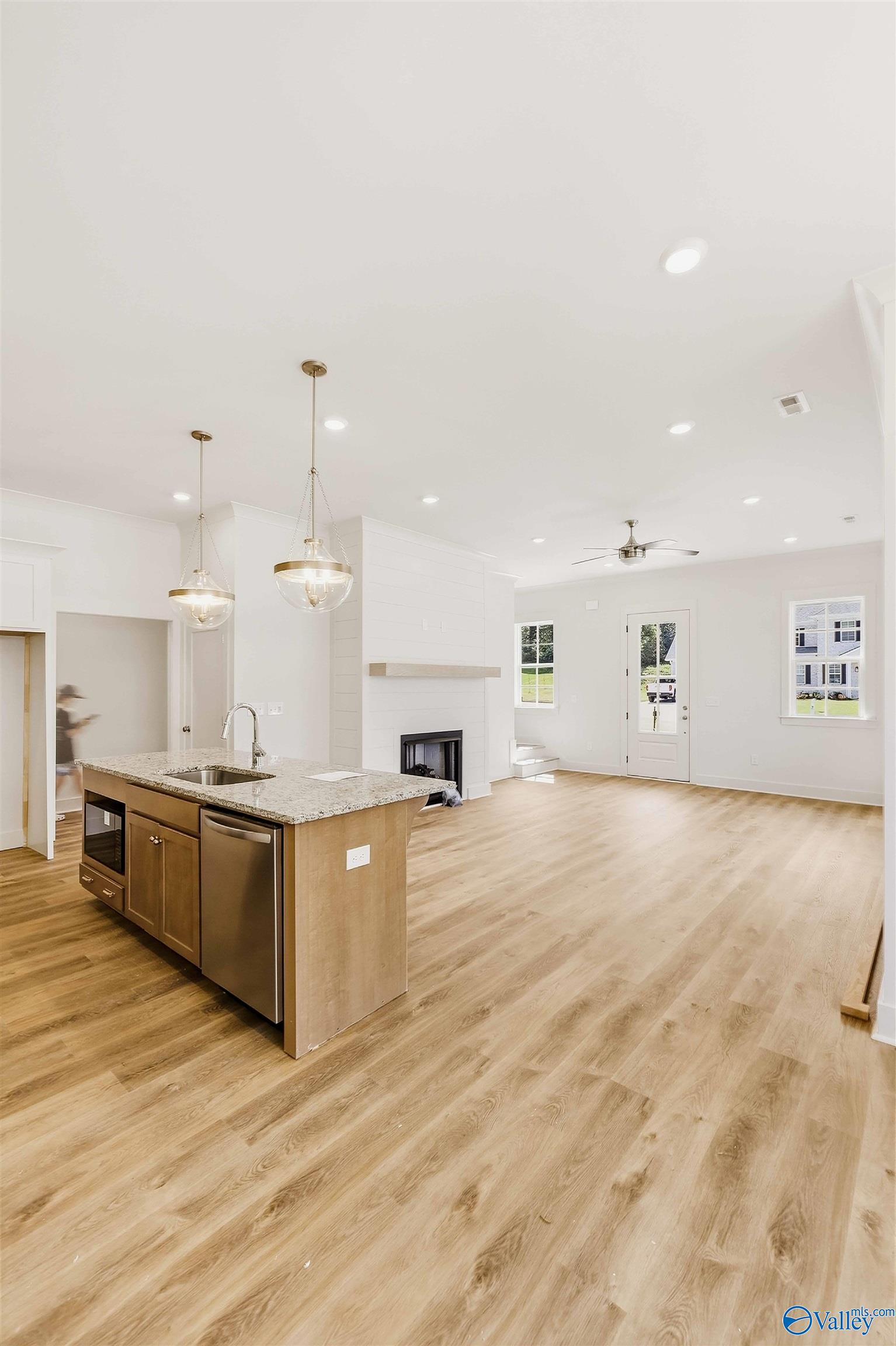 Open kitchen and living area with granite island, wood floors, and white fireplace.