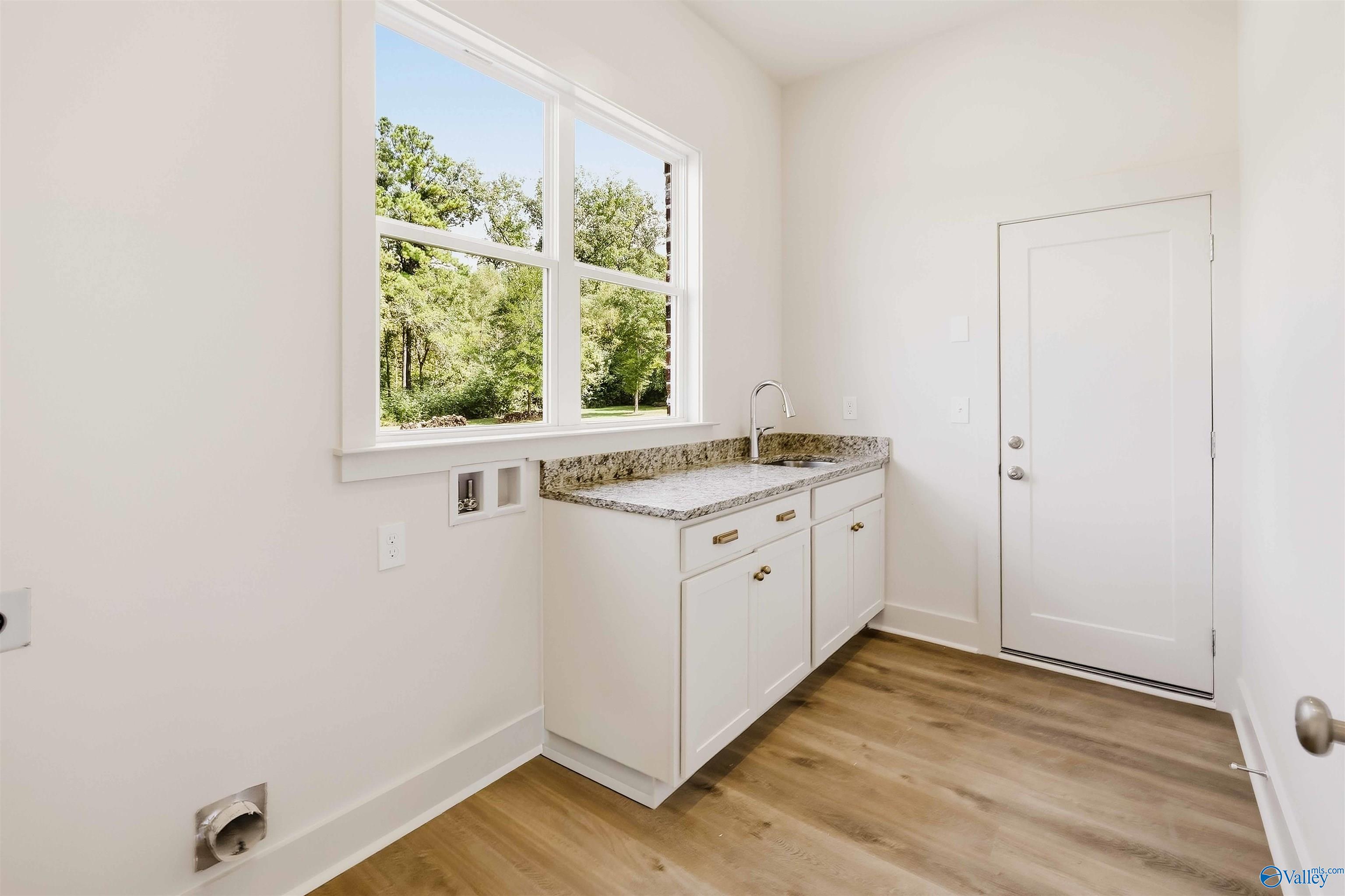 Laundry room with white cabinets, sink, washer hookups, and a large window overlooking trees.