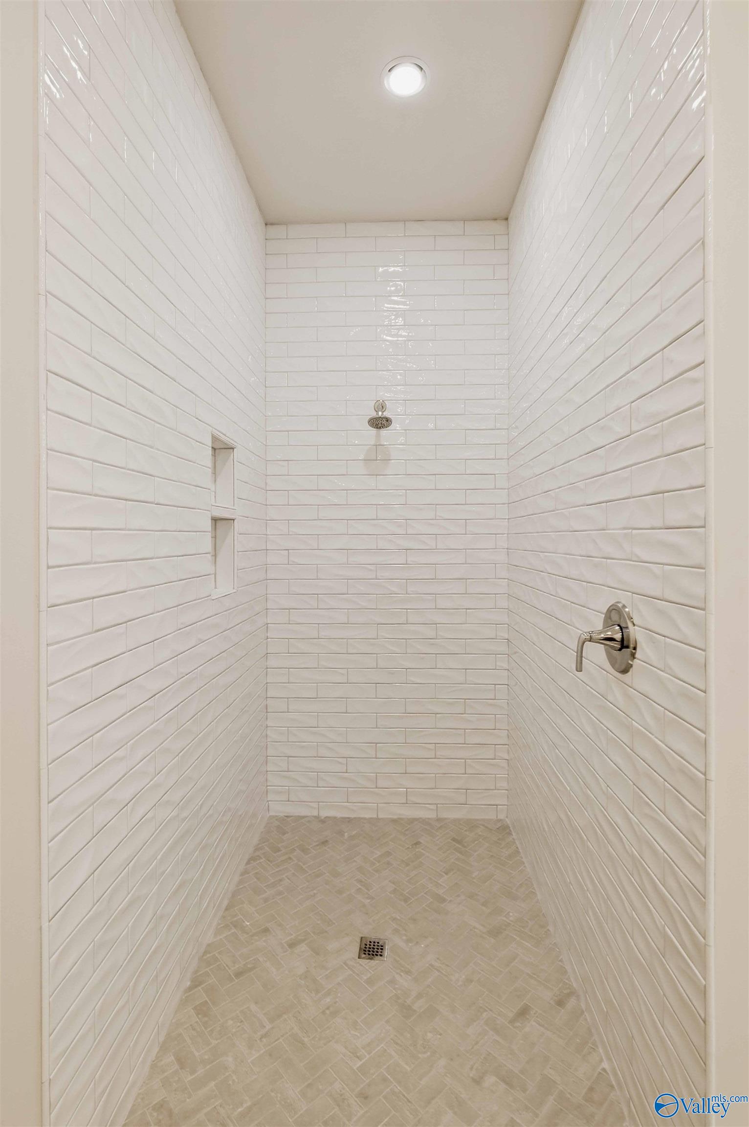 Walk-in shower with white subway tile, a recessed niche, and a herringbone mosaic floor.