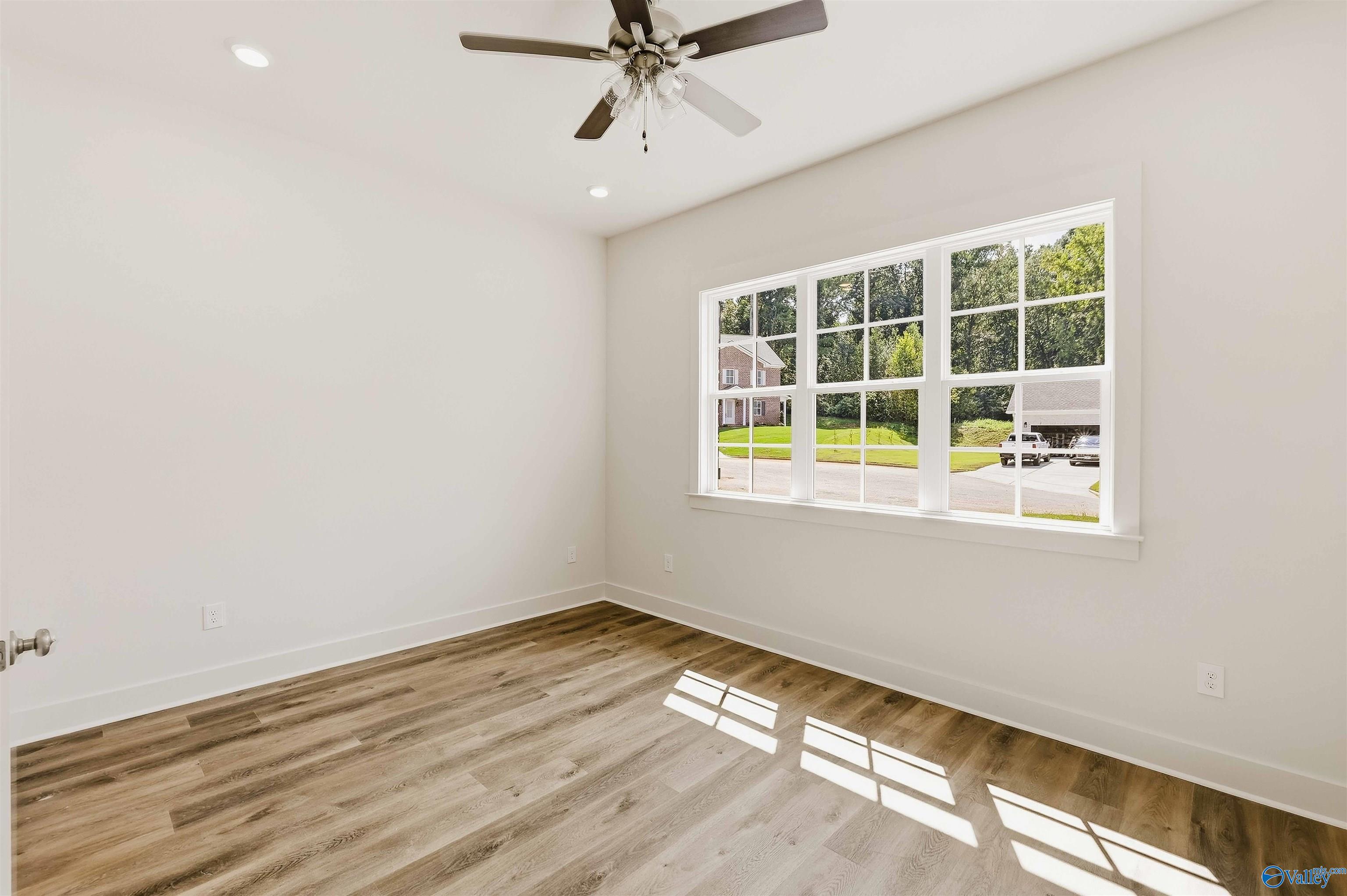 Empty room with wood-look flooring, a ceiling fan, and a large window overlooking the yard.