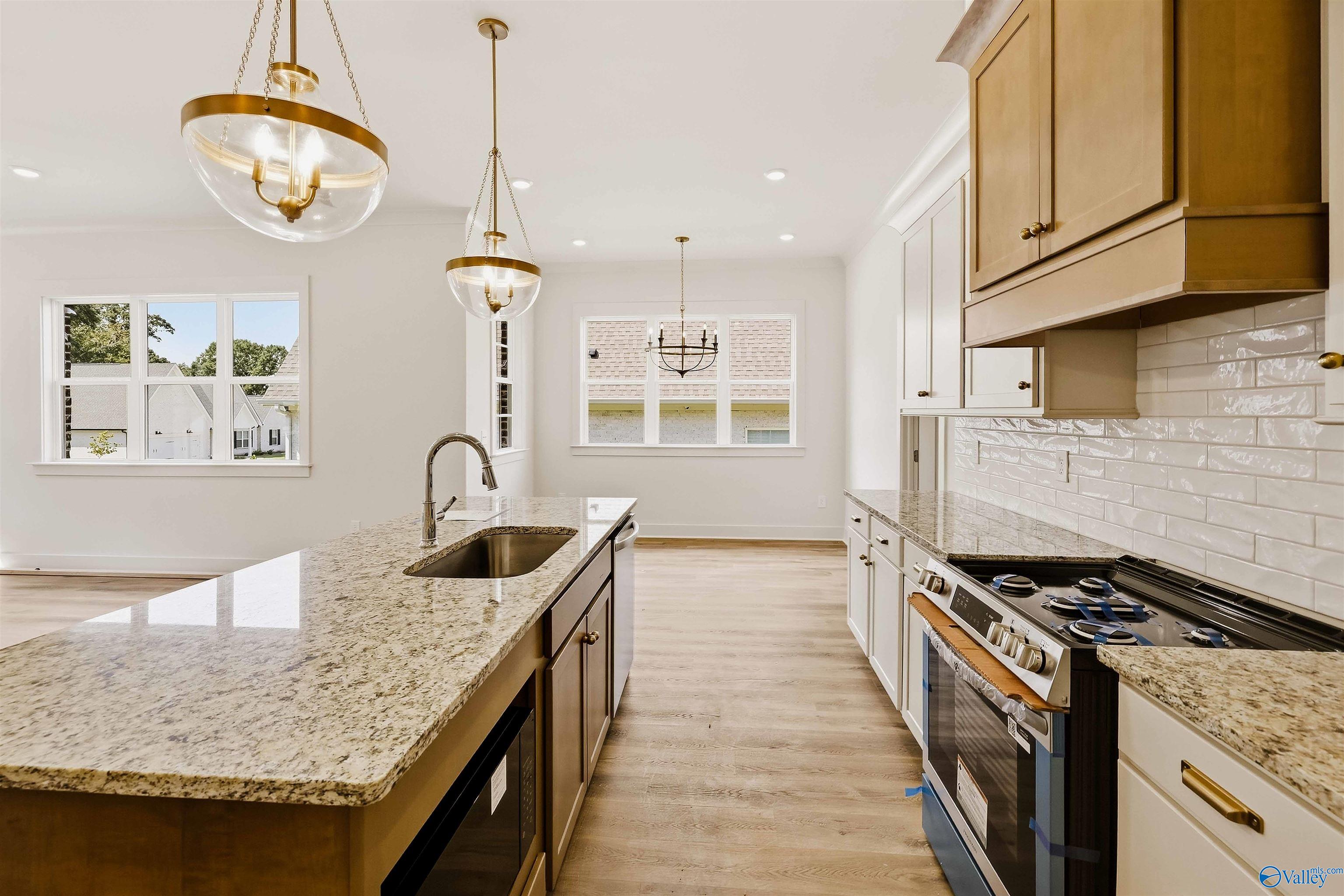 Kitchen with a granite island, tan cabinetry, stainless steel range, and brass pendant lights.