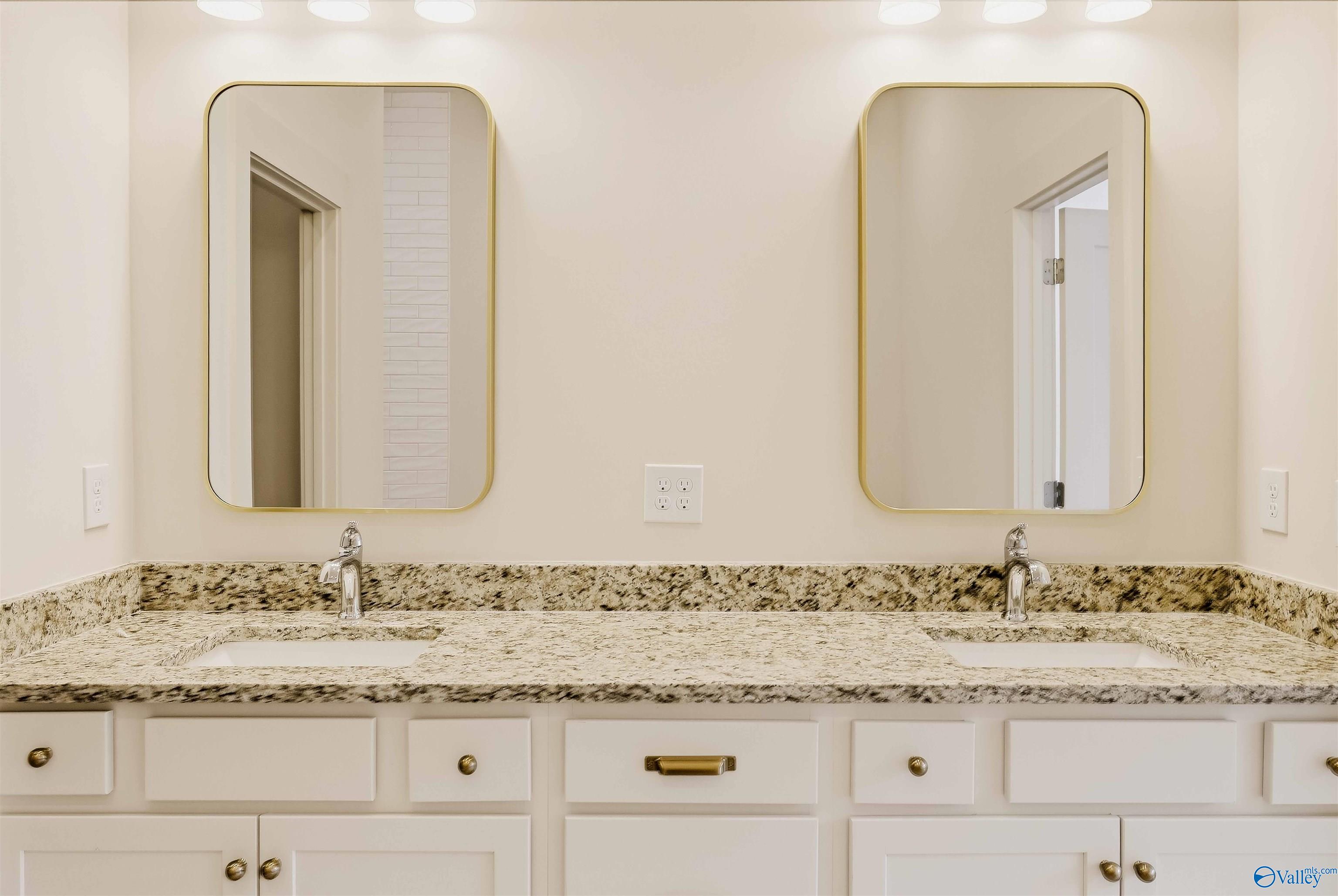 Bathroom double vanity with granite counters, two sinks, and gold-framed mirrors.