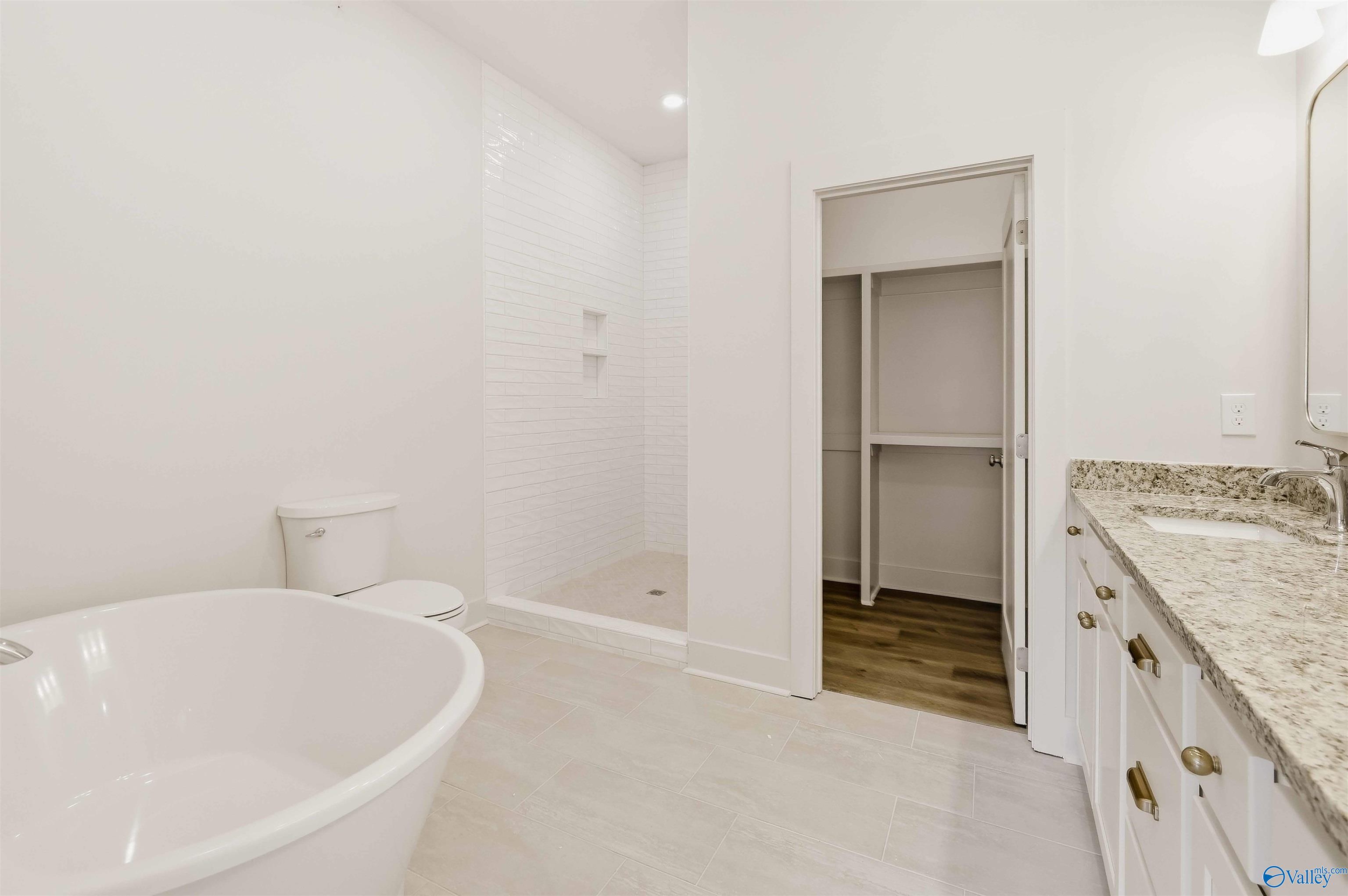 Bathroom with a freestanding tub, tiled walk-in shower, granite vanity, and walk-in closet.