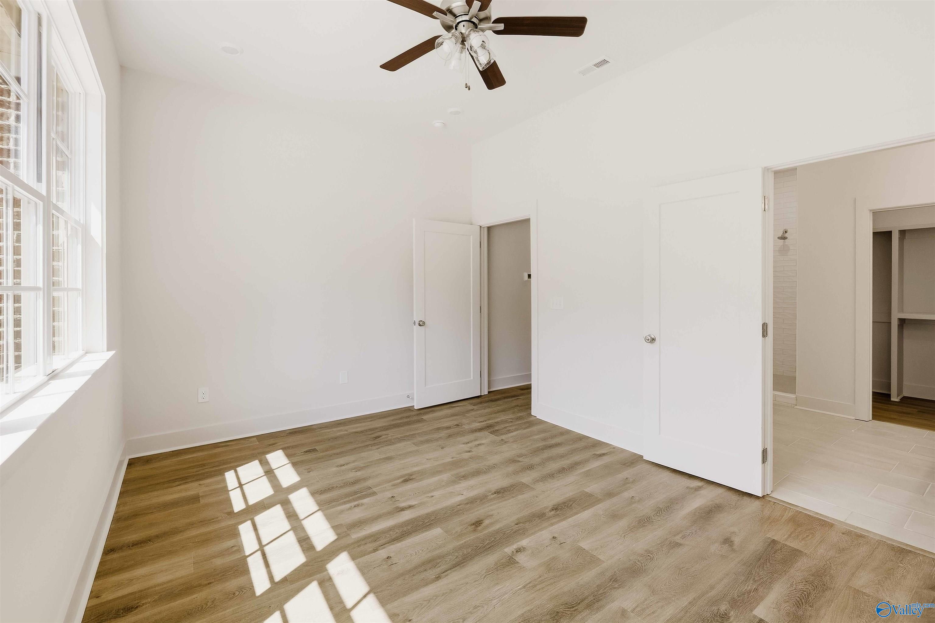 Vacant bedroom with wood-look flooring, a ceiling fan, and large windows.