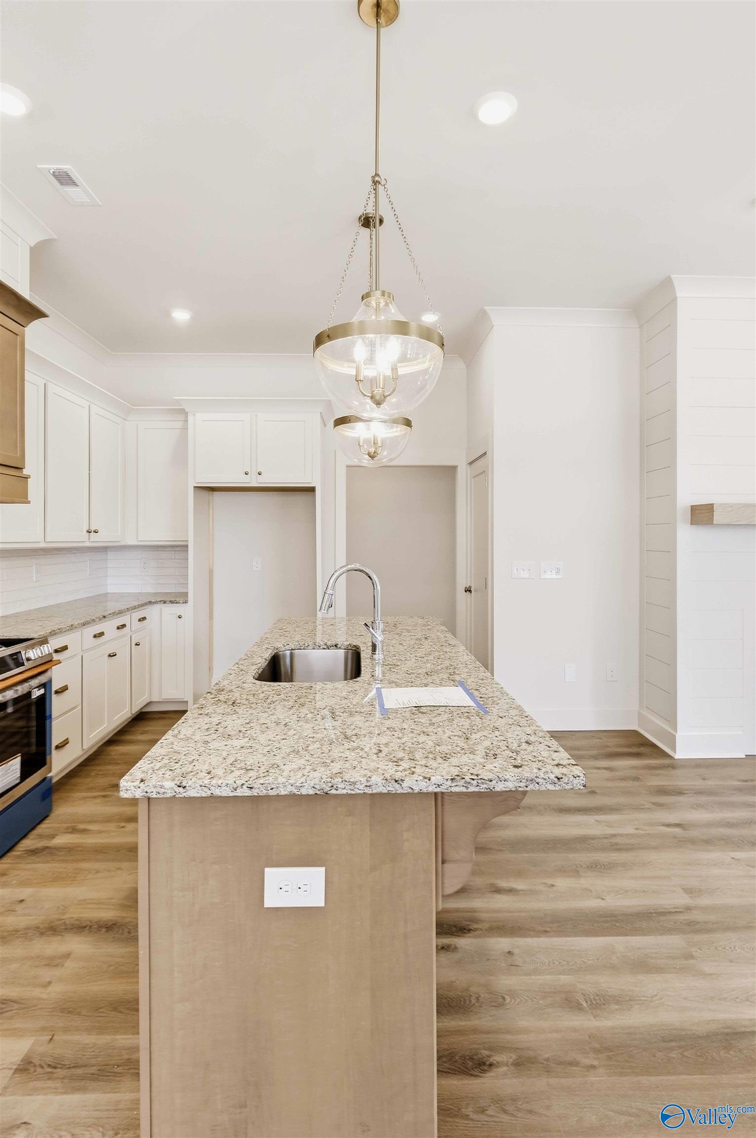 Kitchen with a granite island and sink, white cabinets, brass pendant lights, and wood-look floors.