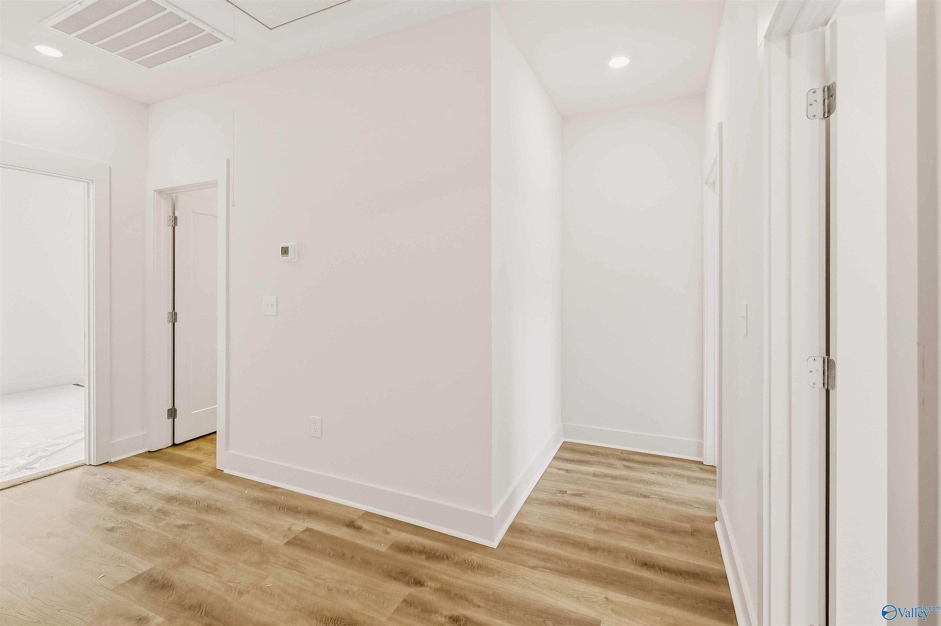 Vacant hallway with white walls, multiple doorways, and wood-look flooring.