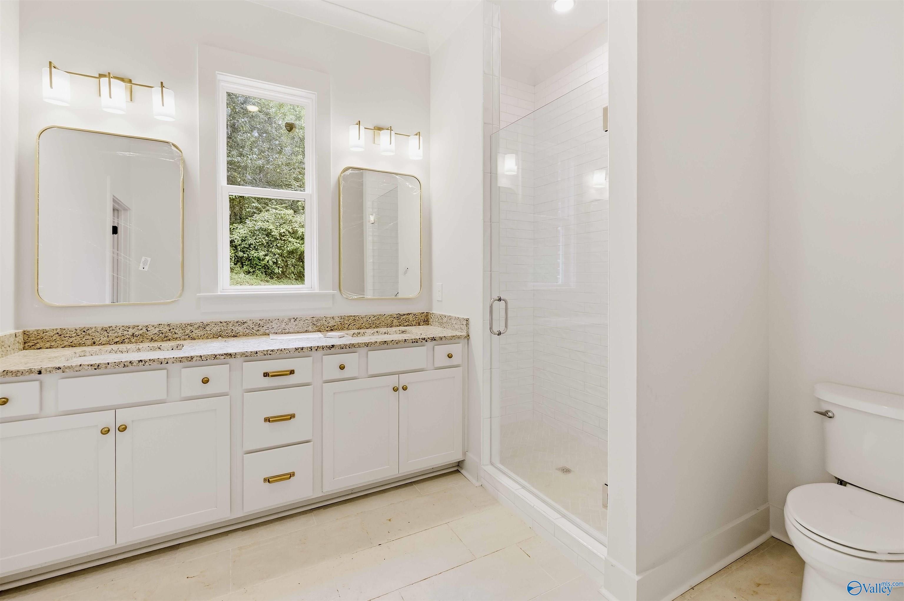 Bright bathroom with a long white vanity, gold-framed mirrors, and a glass-enclosed tiled shower.