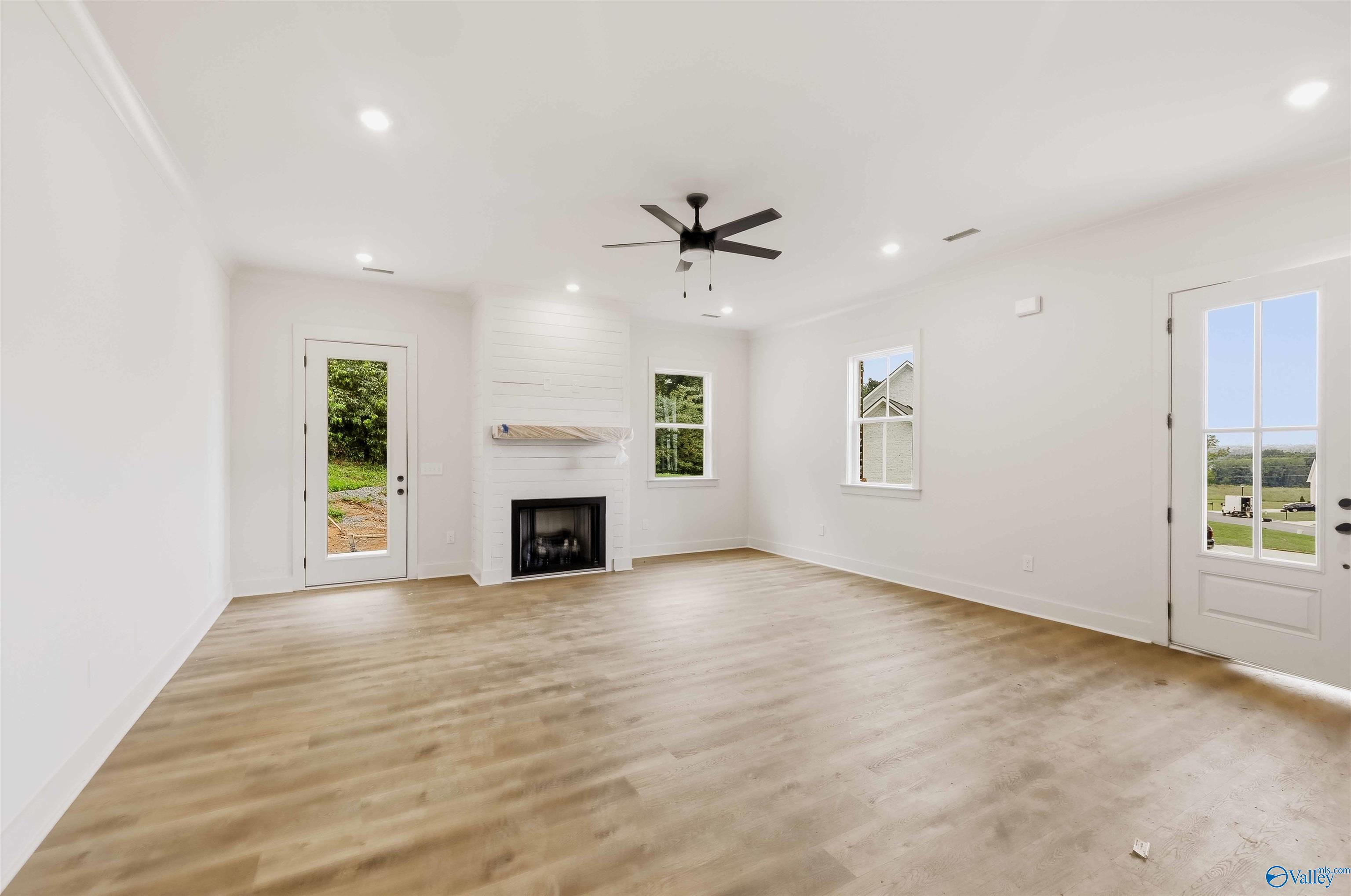 Empty living room with a white fireplace, light wood-look floors, and dark ceiling fan.