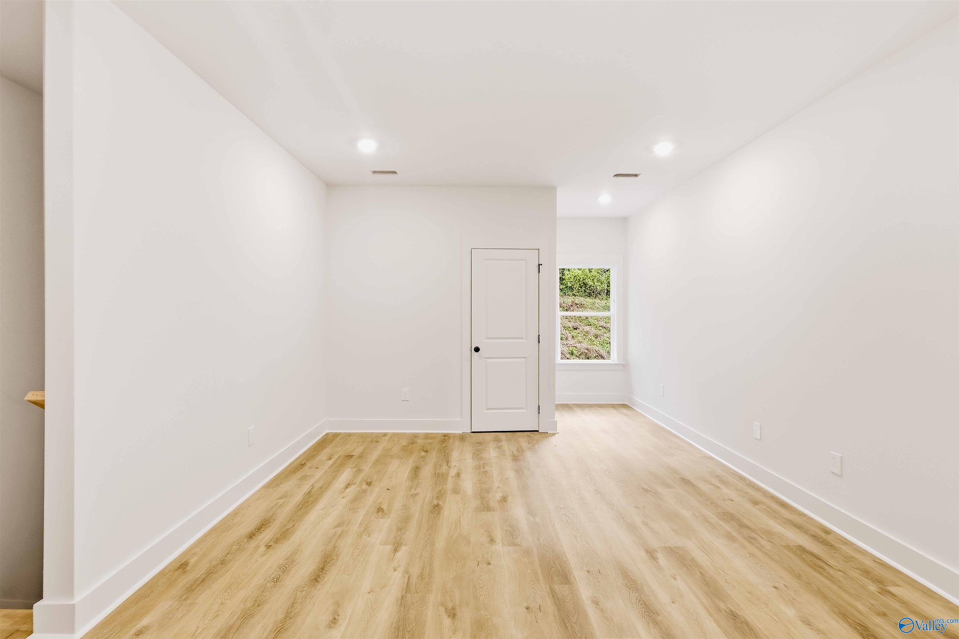 Empty bright room with light wood-look floors, a paneled door, and a window overlooking greenery.