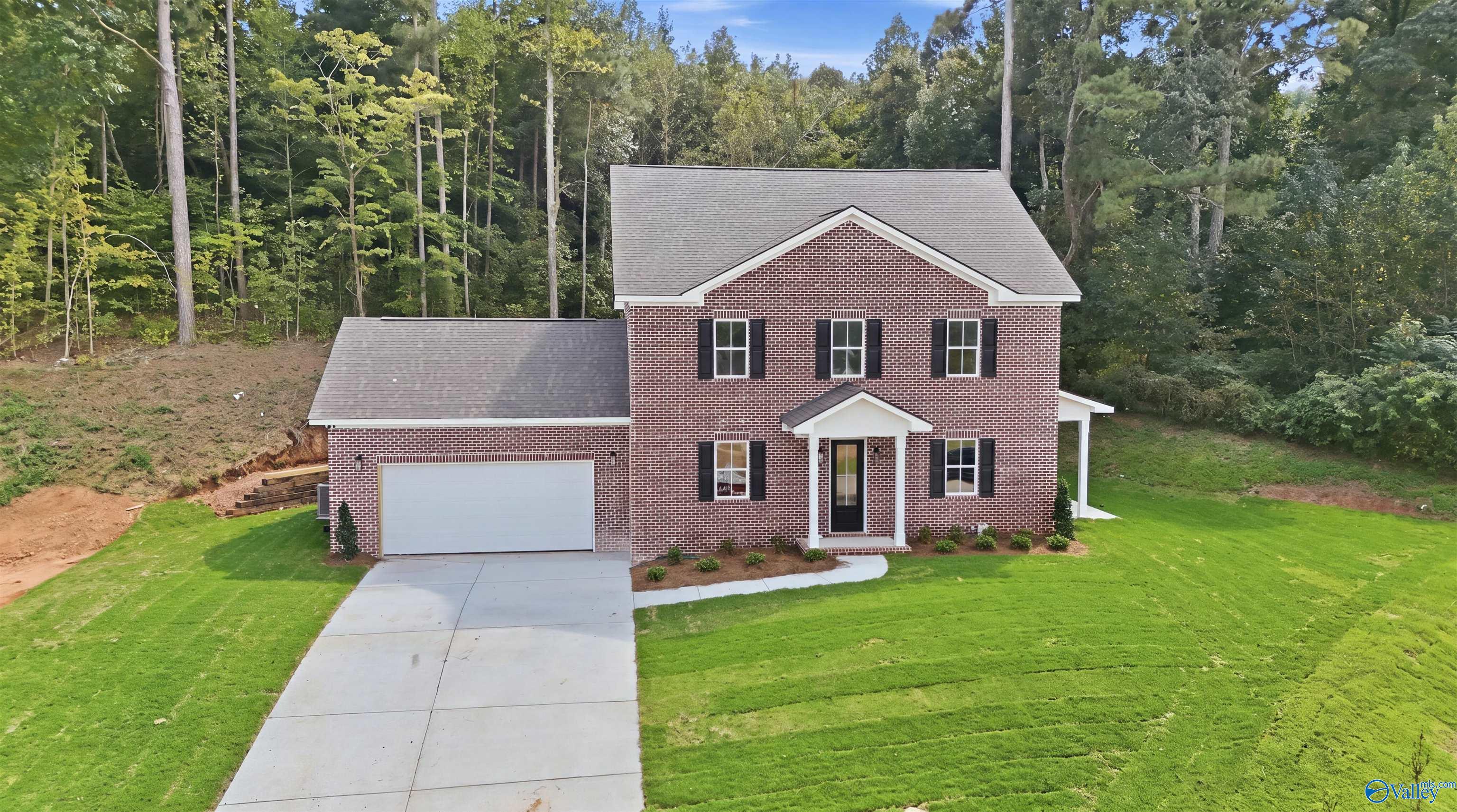 Two-story brick house with an attached garage, driveway, and wooded yard.