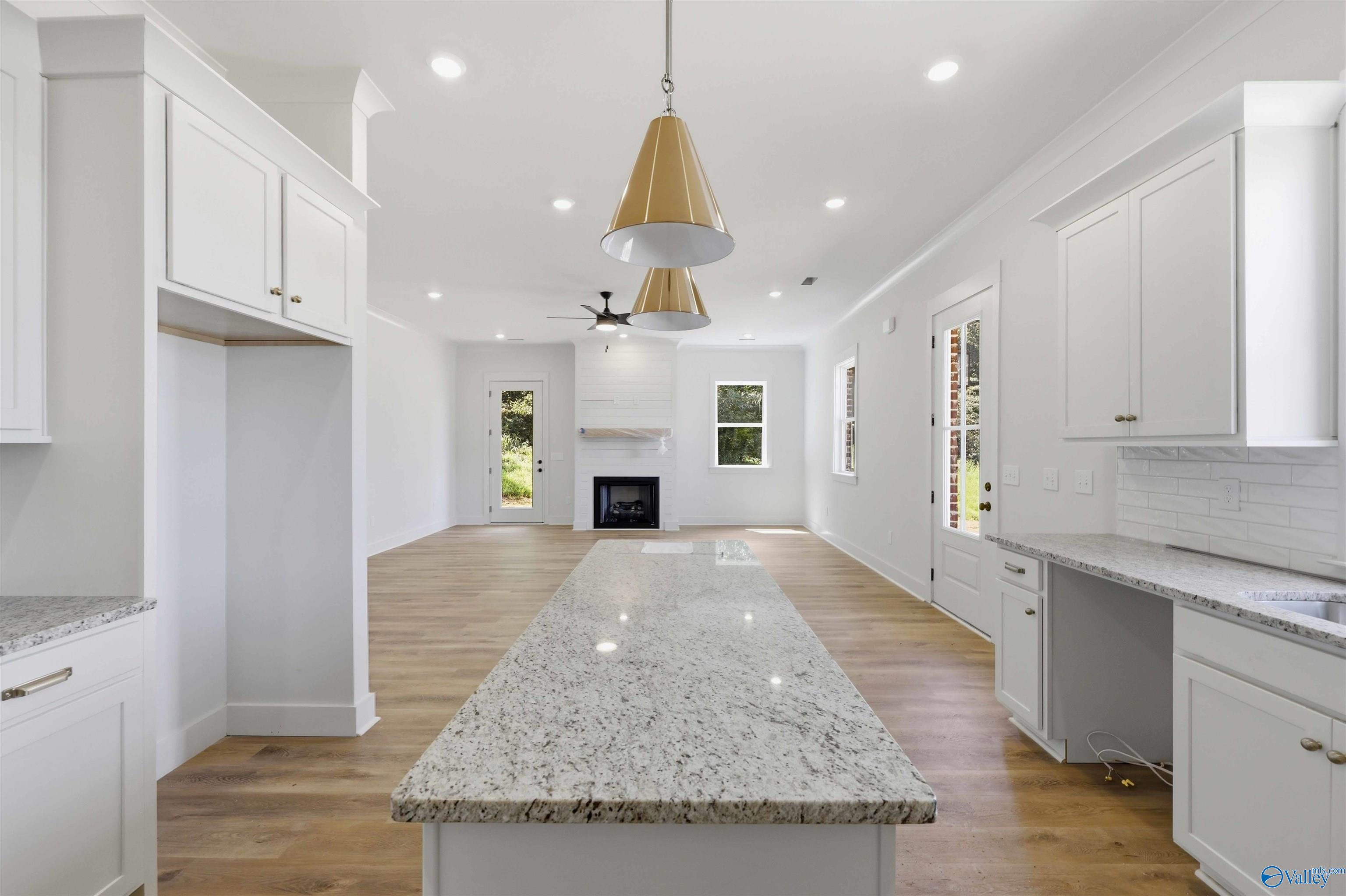 Bright white kitchen with a large stone island and open view of the fireplace living area.