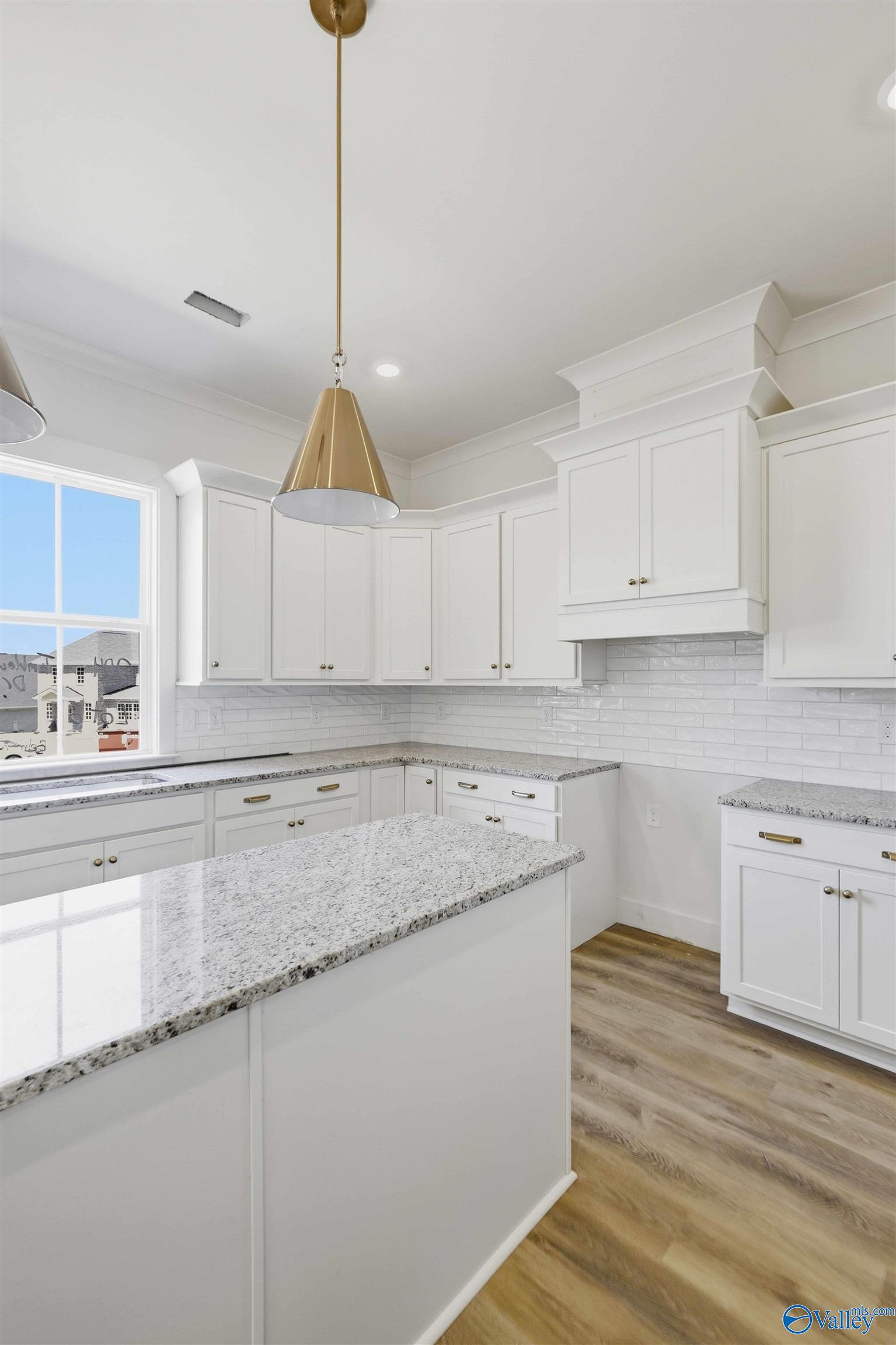 Kitchen with white cabinets, granite island, subway tile backsplash, and brass pendant light.