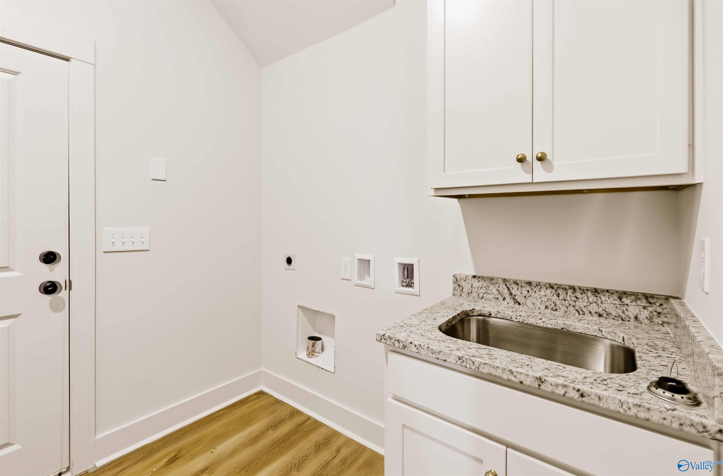 Laundry room with white cabinets, granite counter, stainless steel sink, and washer and dryer hookups.