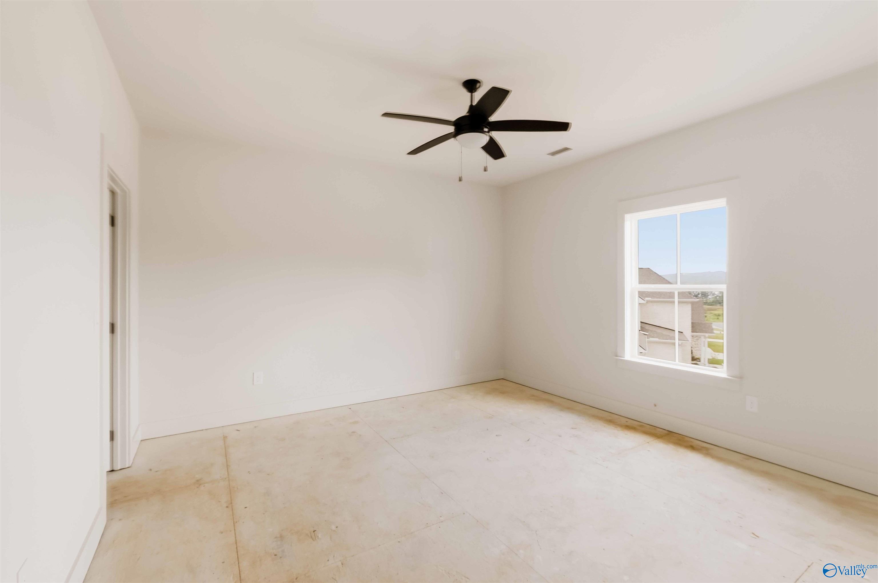 Unfinished empty bedroom with a black ceiling fan and a window overlooking neighboring homes.