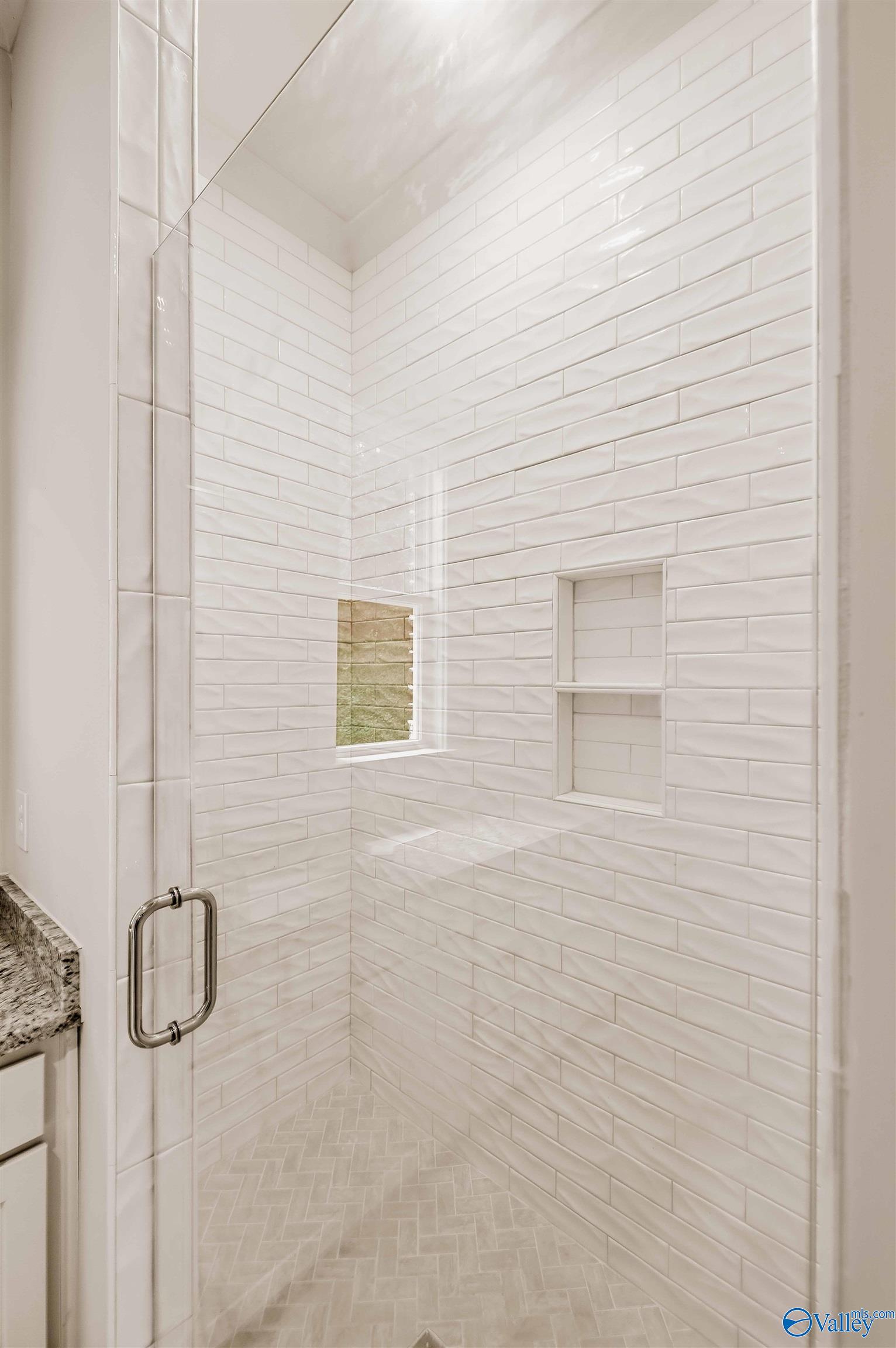 Walk-in shower with white subway tile, recessed niches, a small window, and herringbone flooring.