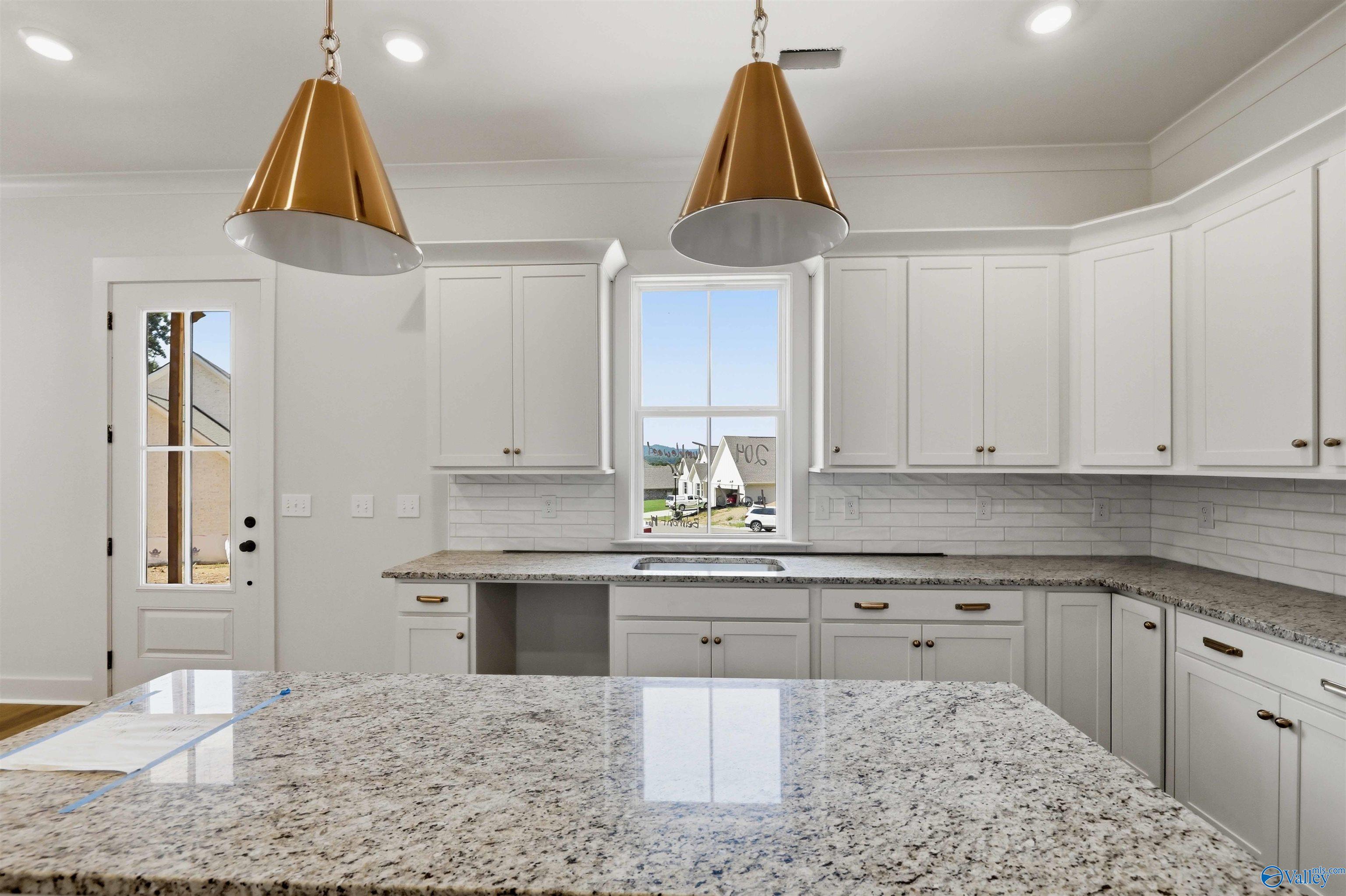 Vacant kitchen with white cabinets, granite counters, a large island, and copper-colored pendant lights.