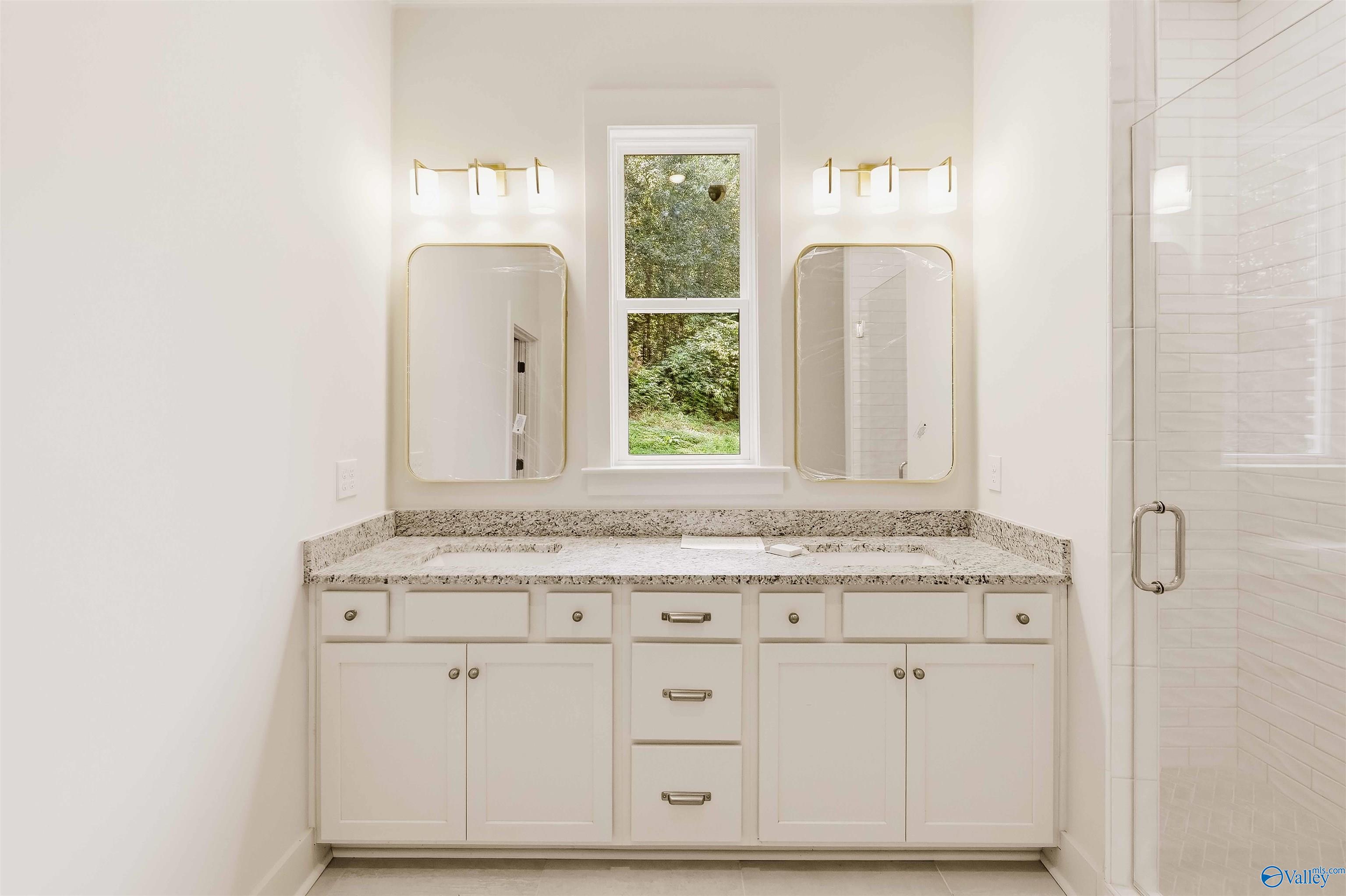 Bathroom with a white double vanity, granite countertop, twin mirrors, and a window overlooking greenery.