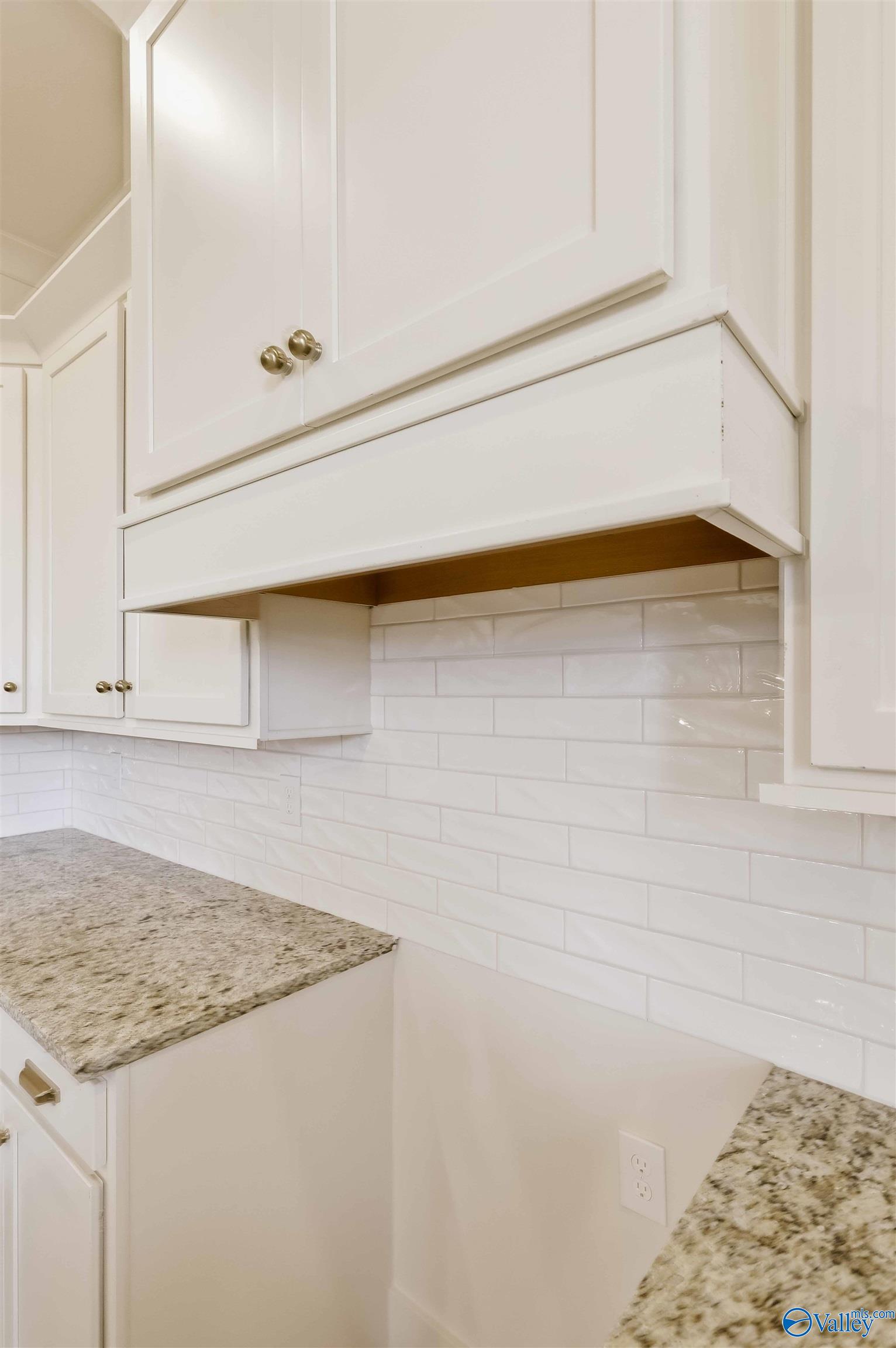 Kitchen with white cabinets, a built-in hood, glossy subway-tile backsplash, and speckled granite countertops.