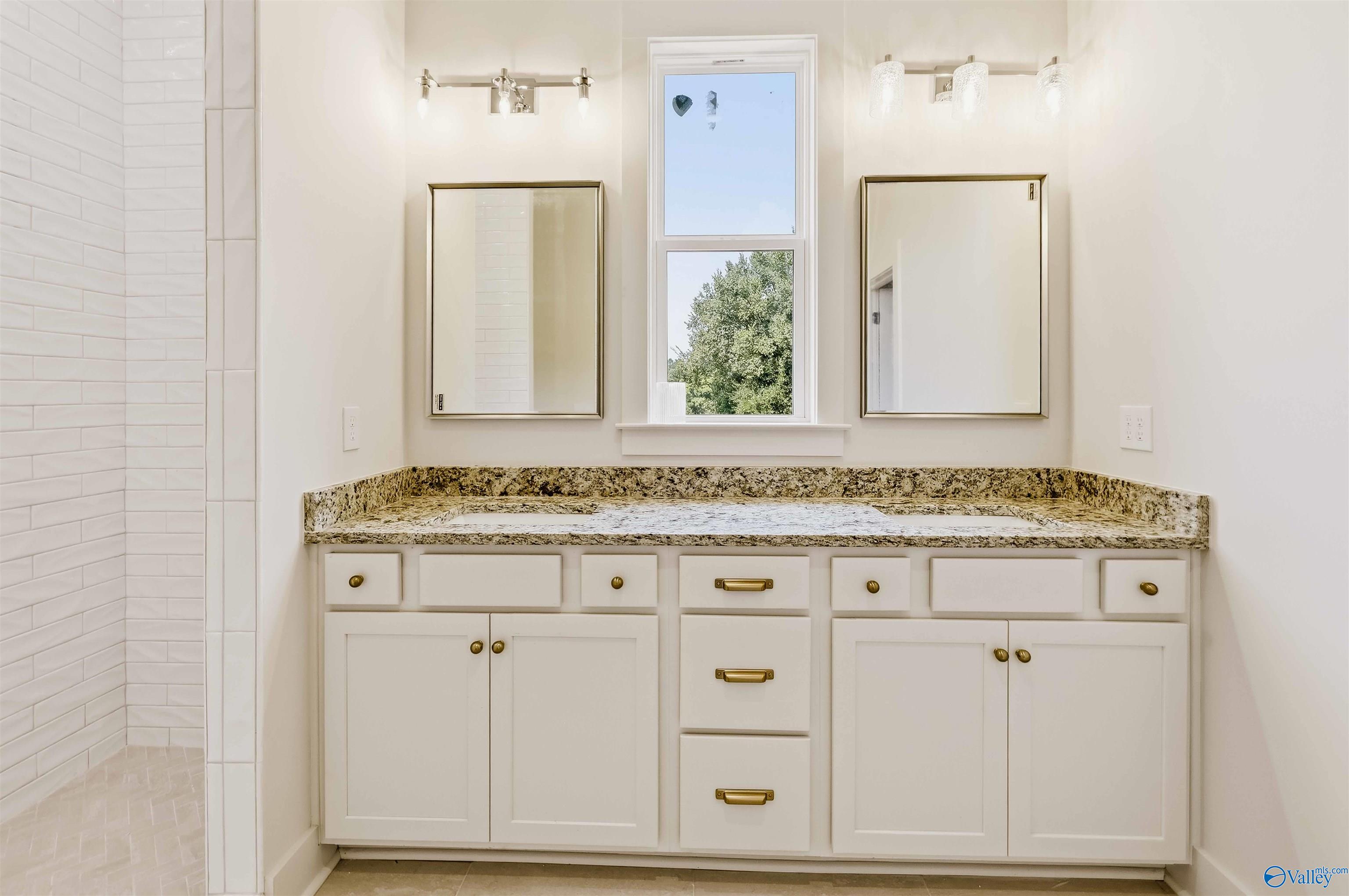 Bathroom vanity with speckled granite countertop, white cabinetry, two framed mirrors, and a tall window.