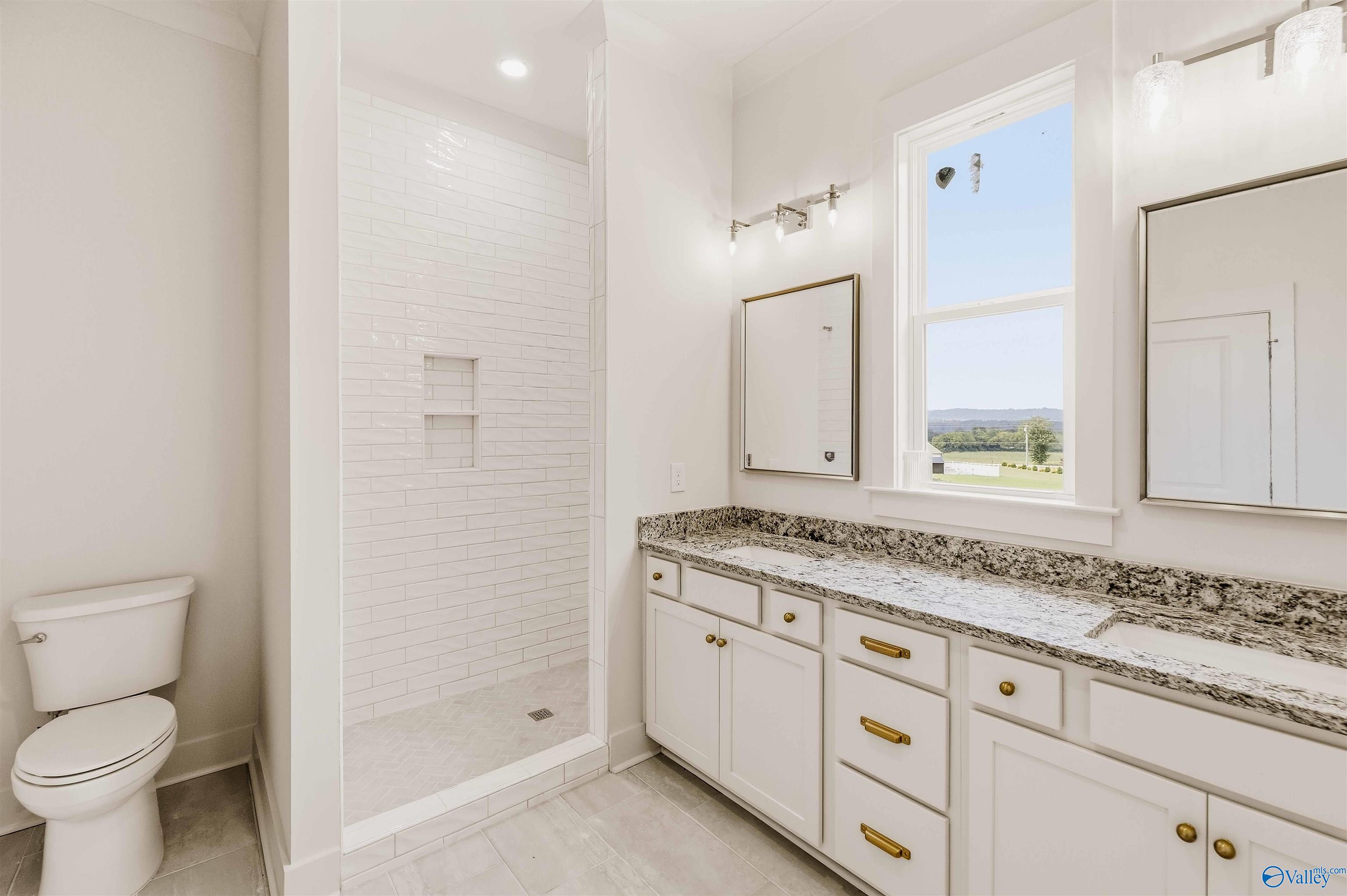 Bathroom with a tiled walk-in shower, long white vanity, brass hardware, and a valley view through the window.