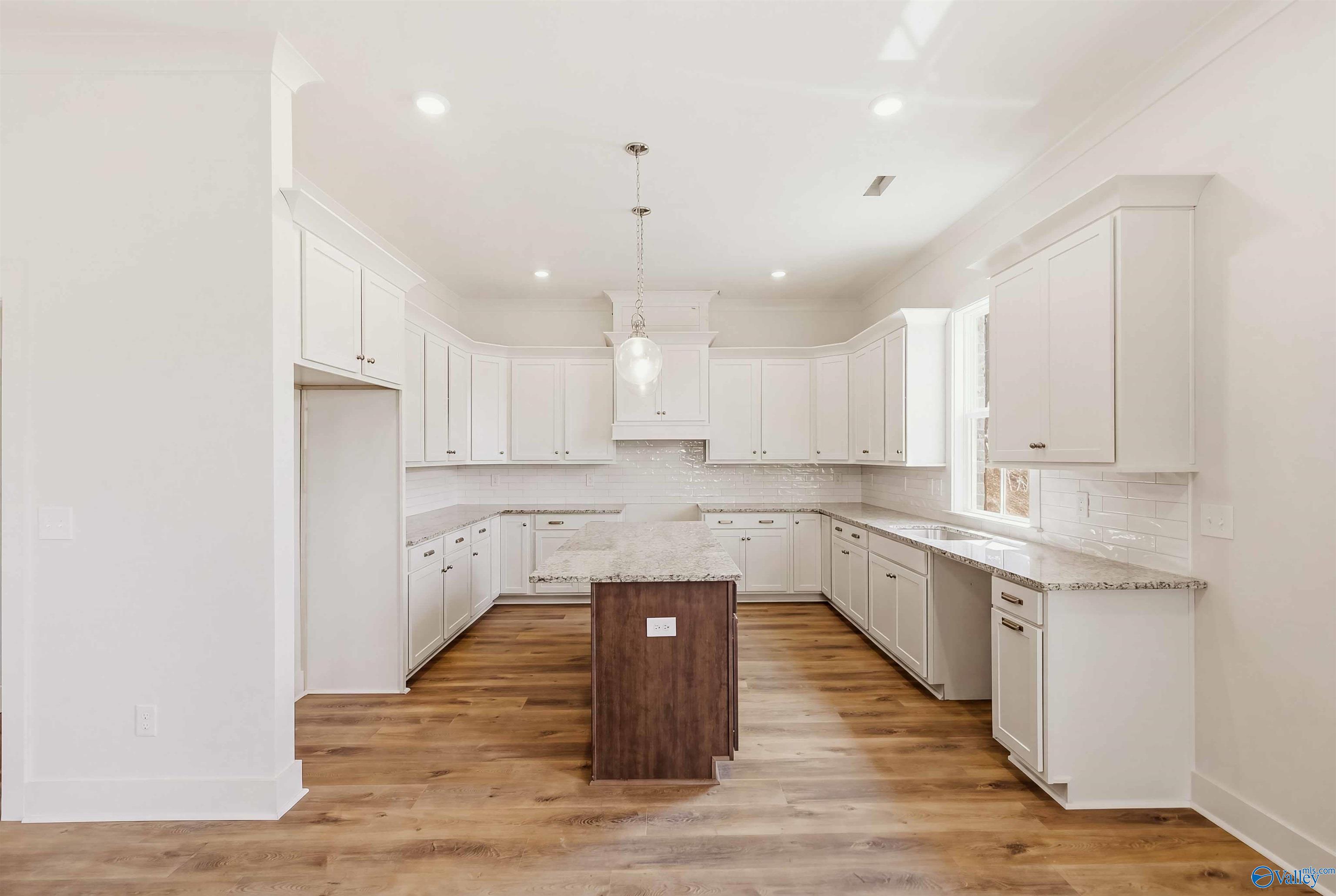 Kitchen with white cabinets, granite counters, a dark wood island, and warm wood-look flooring.