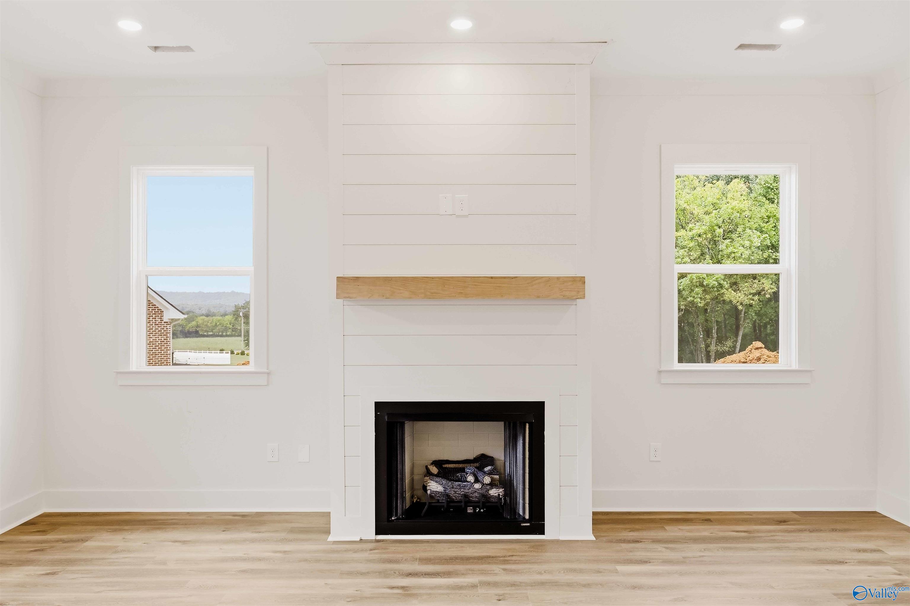 Vacant living room with a white shiplap fireplace, natural wood mantel, and two windows.