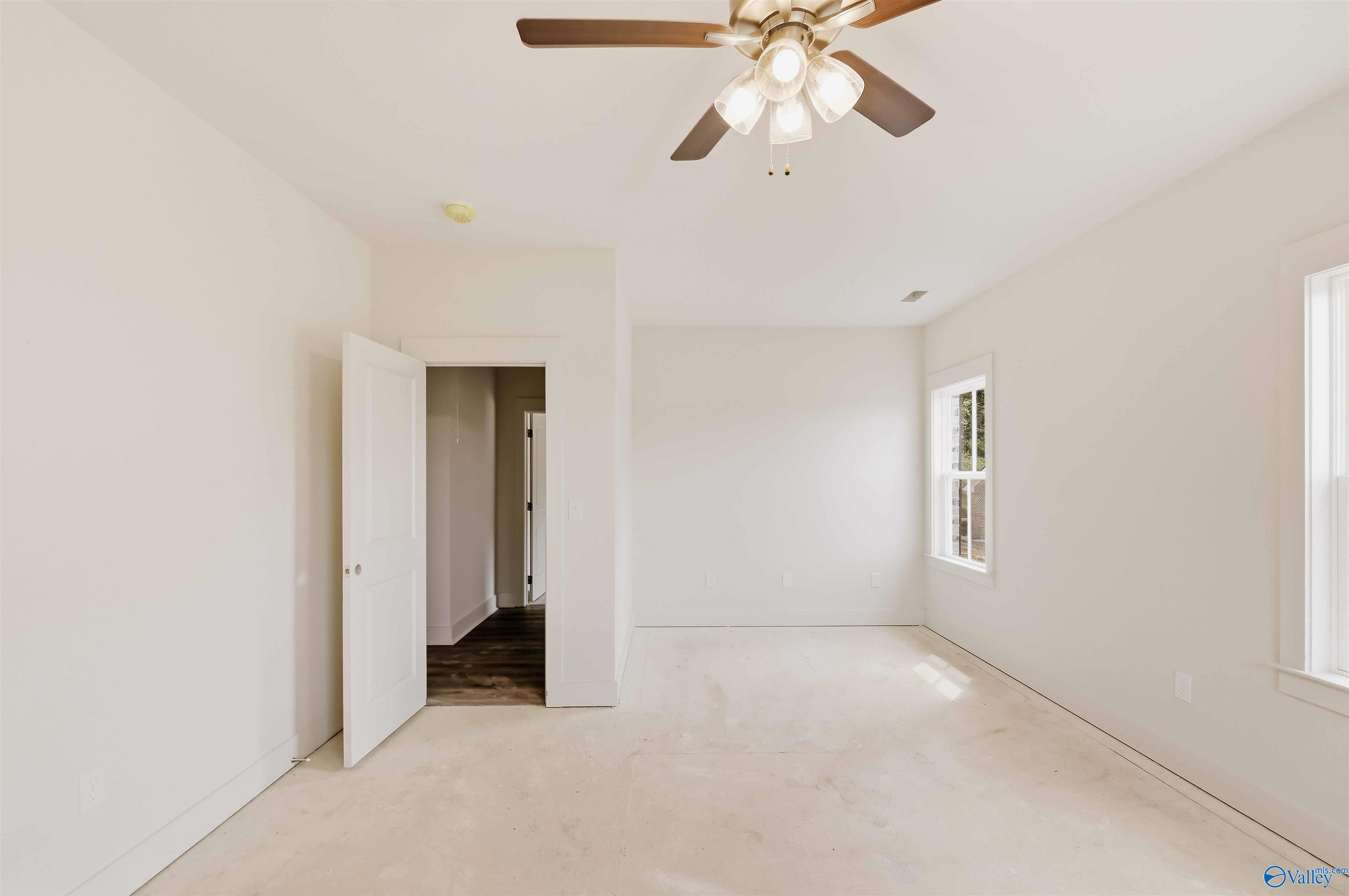 Empty bright room with a ceiling fan, two windows, and an open doorway to a hallway.
