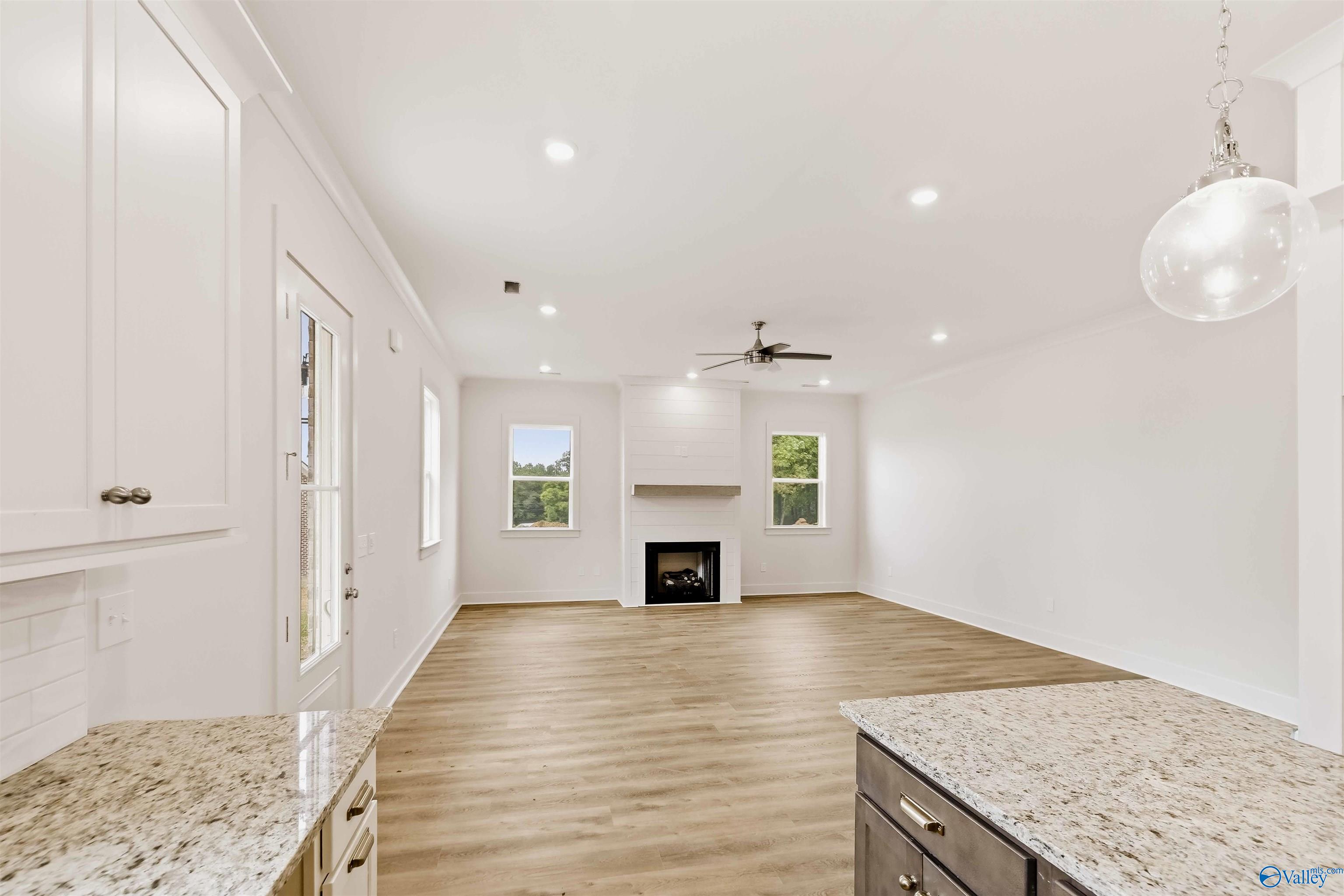 Open kitchen and living area with stone counters, wood-look floors, and a white fireplace.